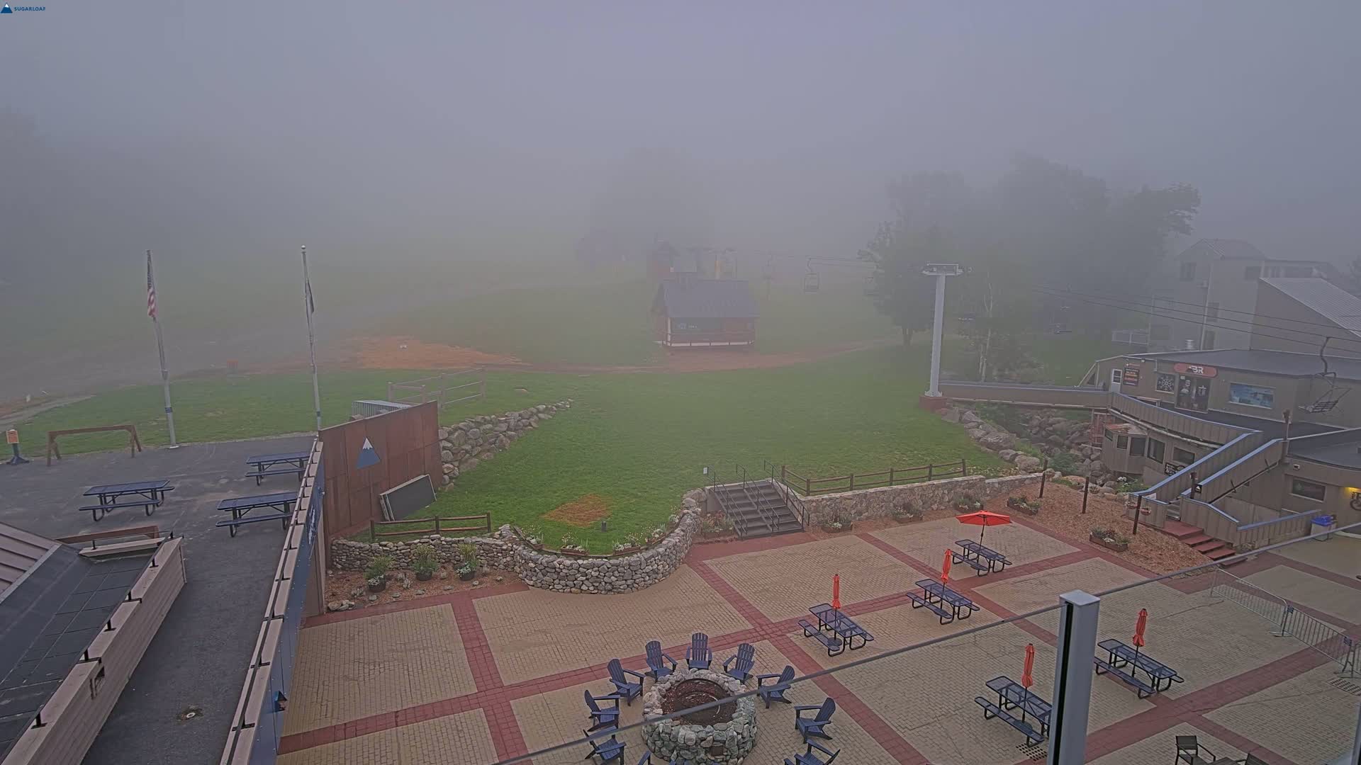 A foggy outdoor patio area with picnic tables, a fire pit, and a building in the background.