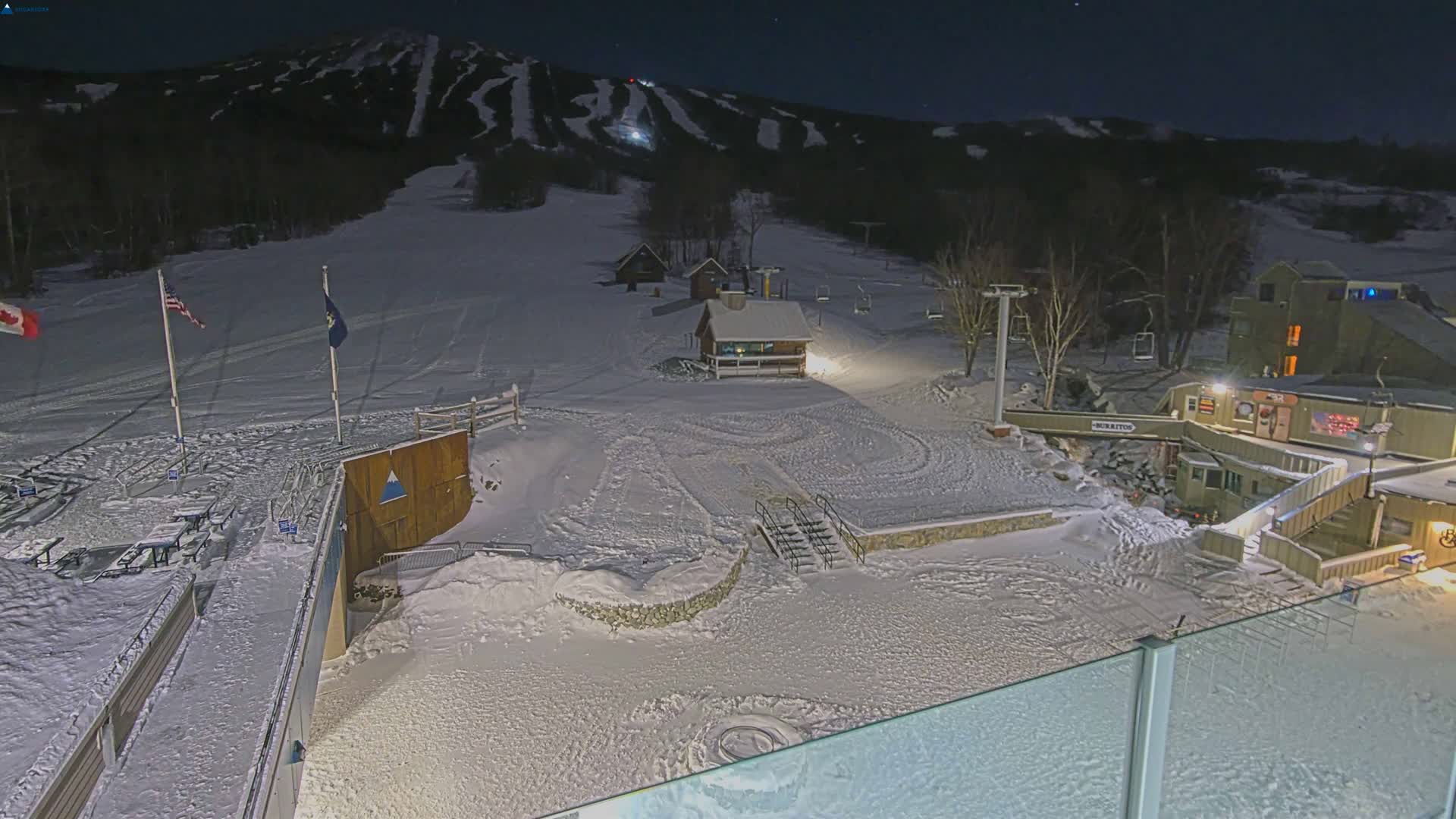A clear, cold winter night scene at a snow-covered mountain ski resort reveals illuminated slopes, multiple buildings, and ski lifts under a starry sky.