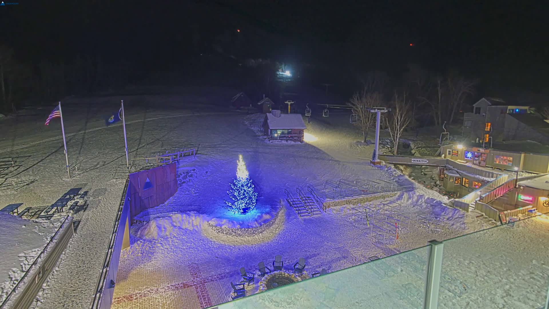 A clear, cold winter night scene at a snow-covered mountain ski resort reveals illuminated slopes, multiple buildings, and ski lifts under a starry sky.