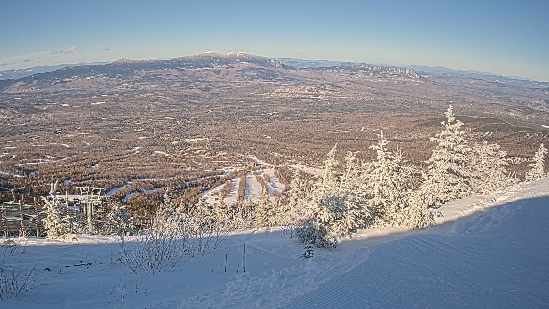 A snow-covered ski resort valley is seen from a snowy mountaintop on a clear, sunny day.