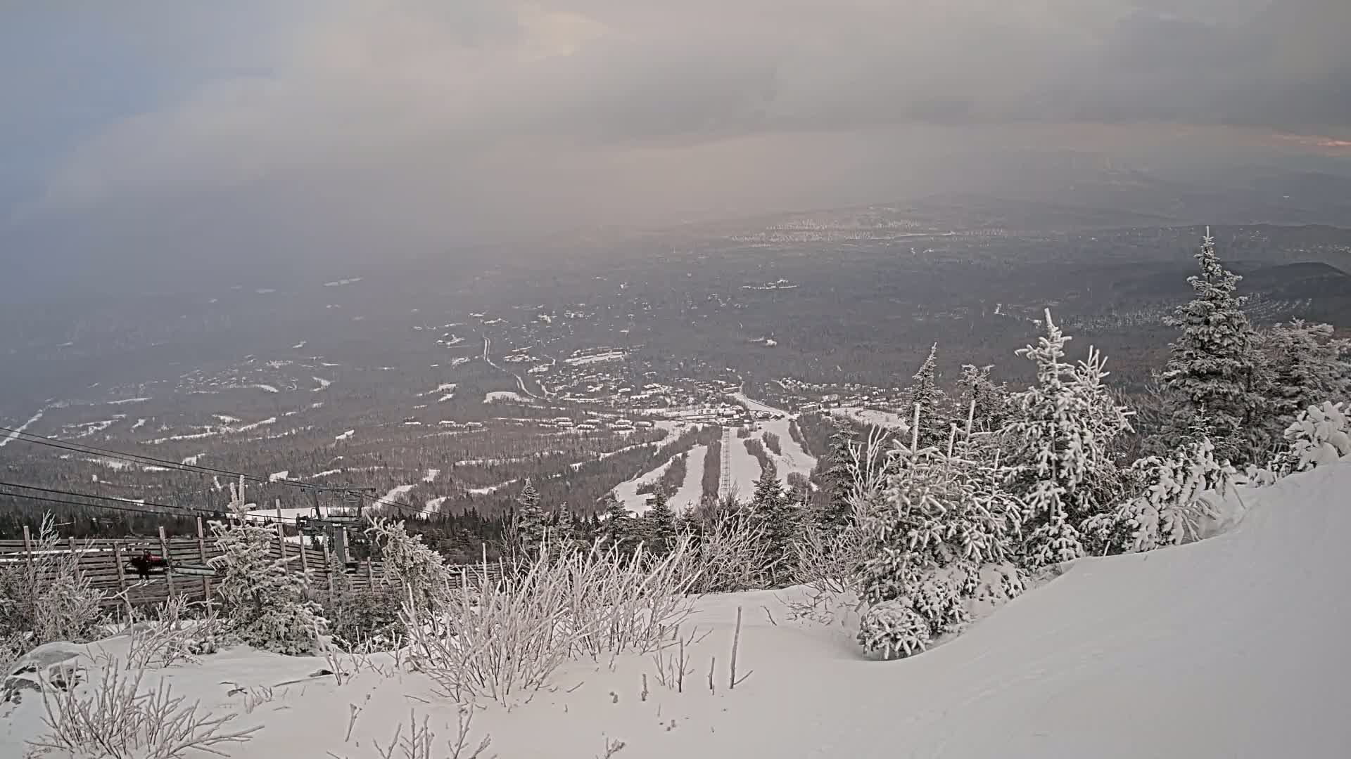 A snowy landscape with a view of a ski resort valley under an overcast sky.