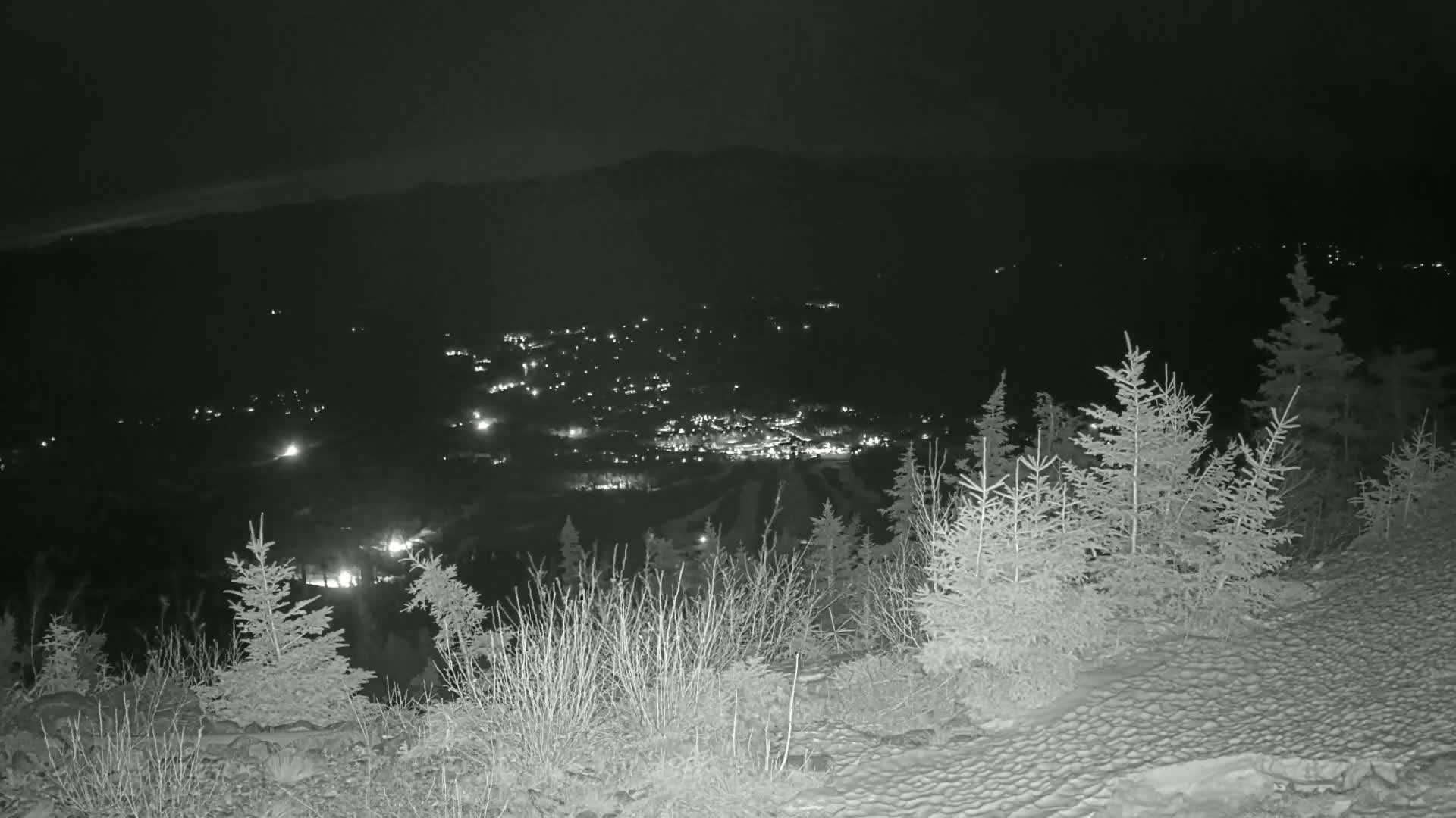 A nighttime view from a snow-covered hilltop shows a valley with a town illuminated by scattered lights.