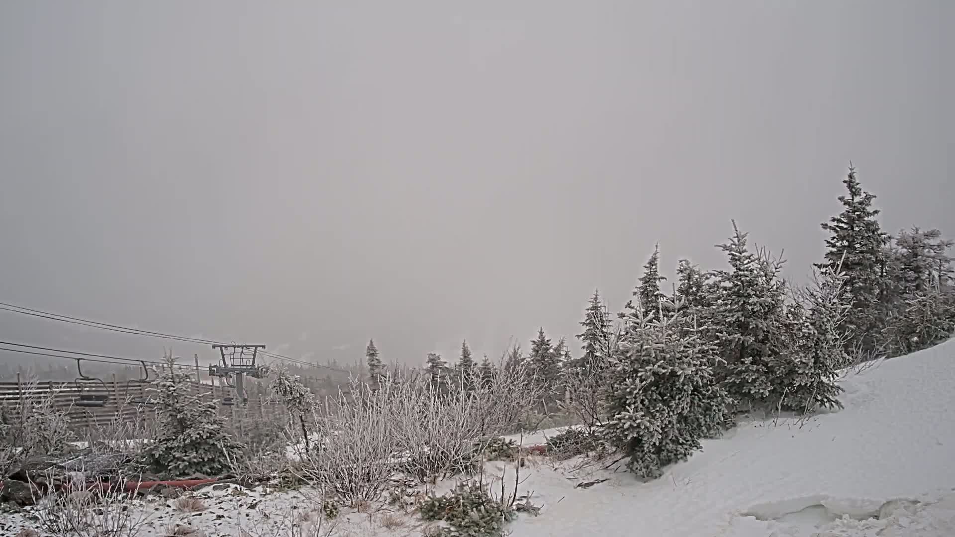 A snow-covered landscape with evergreen trees and a ski lift is visible under a heavy gray sky.
