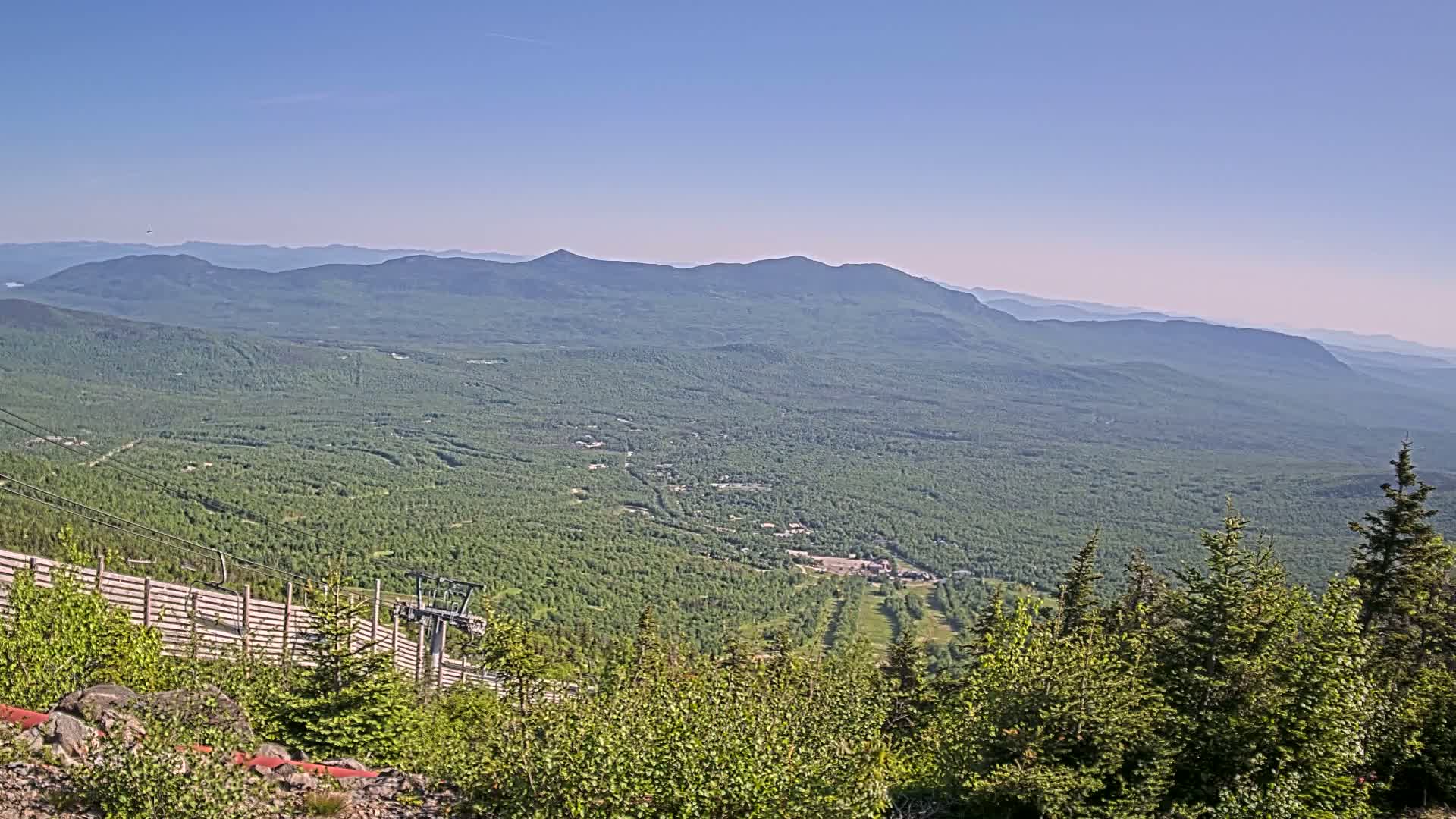 A vast expanse of green mountains and forests stretches to the horizon under a clear blue sky.