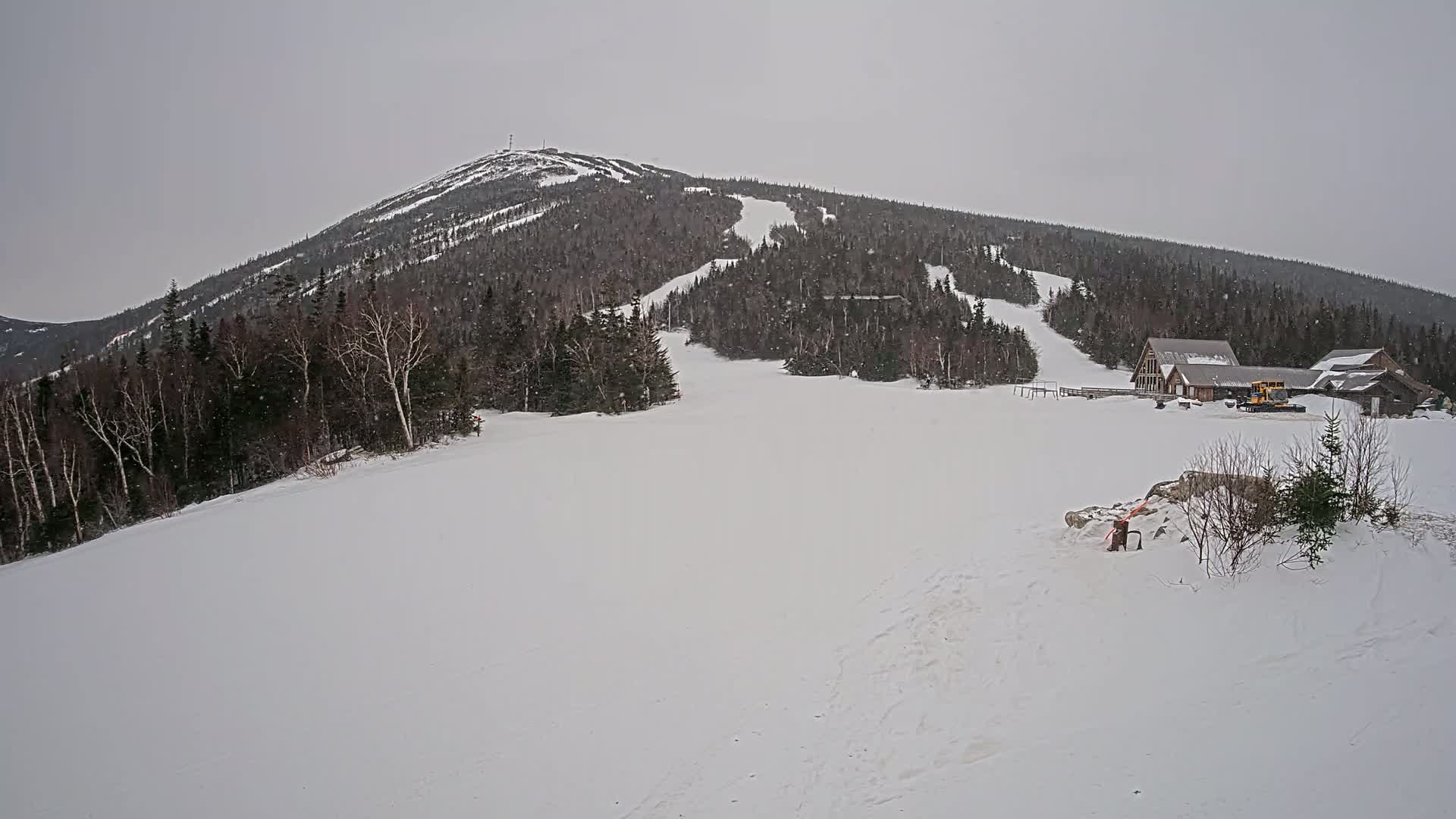 A snow-covered ski slope at the base of a mountain under a gray, overcast sky.