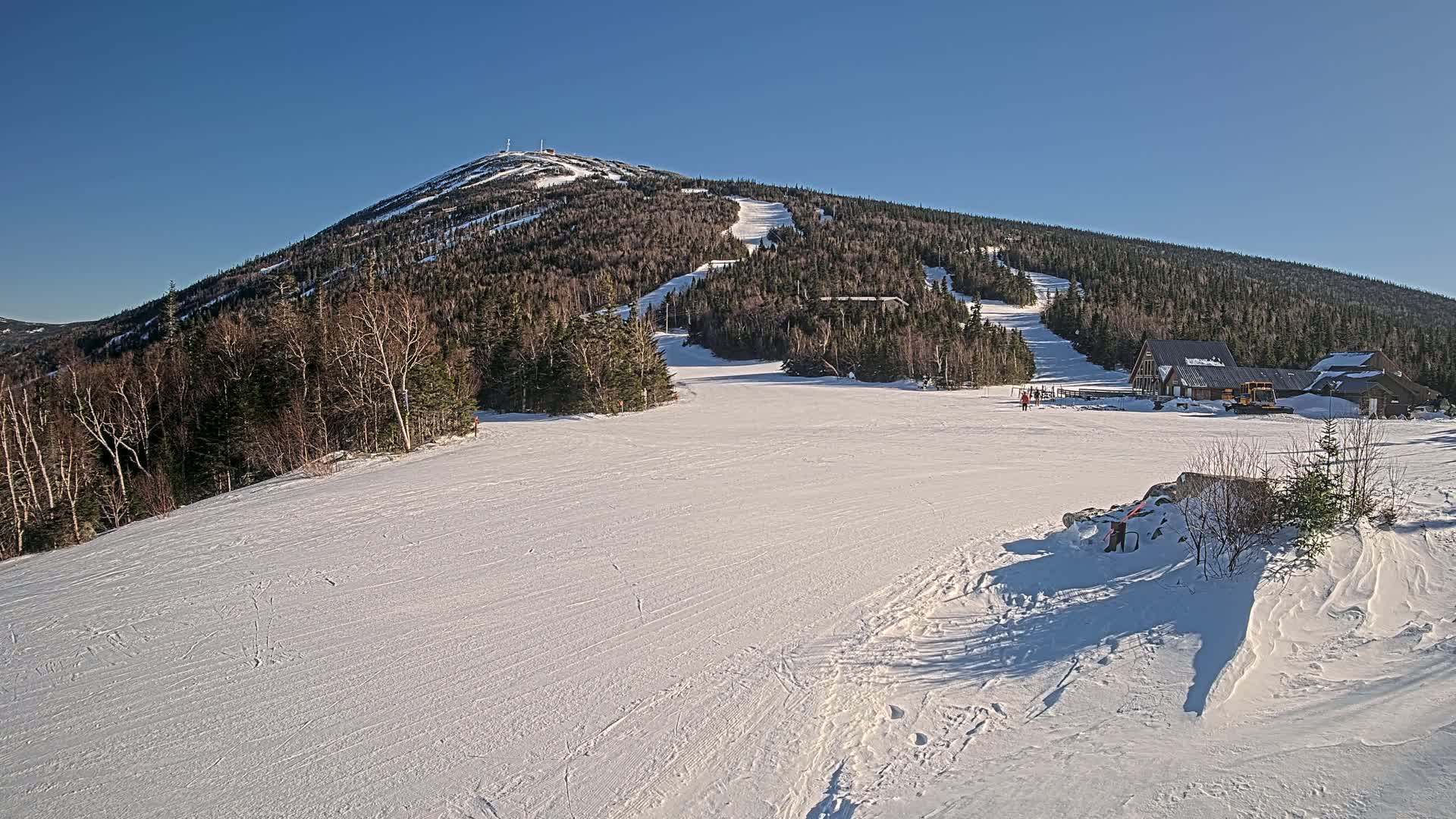 A snow-covered ski slope with a mountain in the background under clear blue skies.
