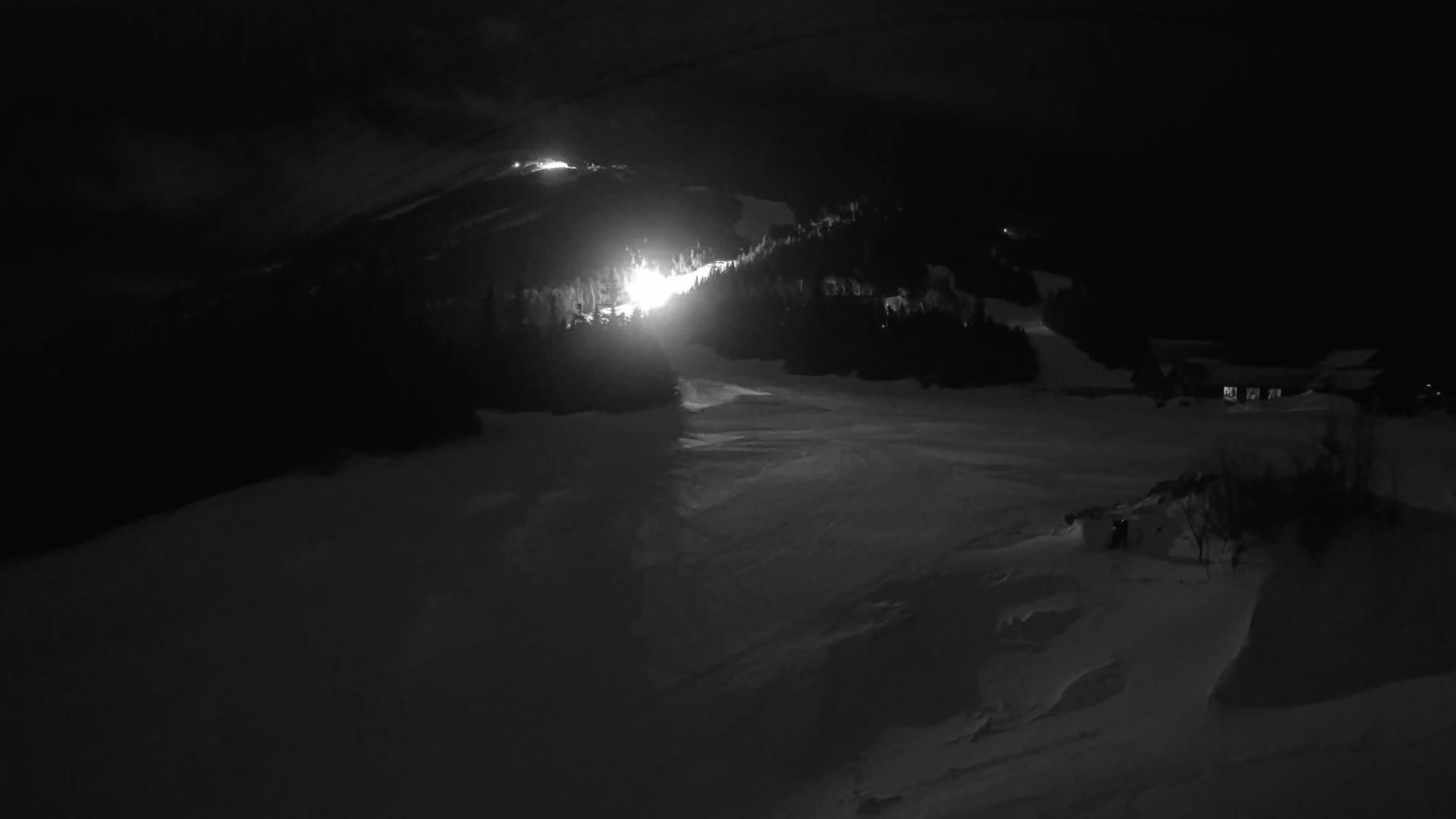 A brightly lit ski slope is visible at night in a snow-covered mountainous area.