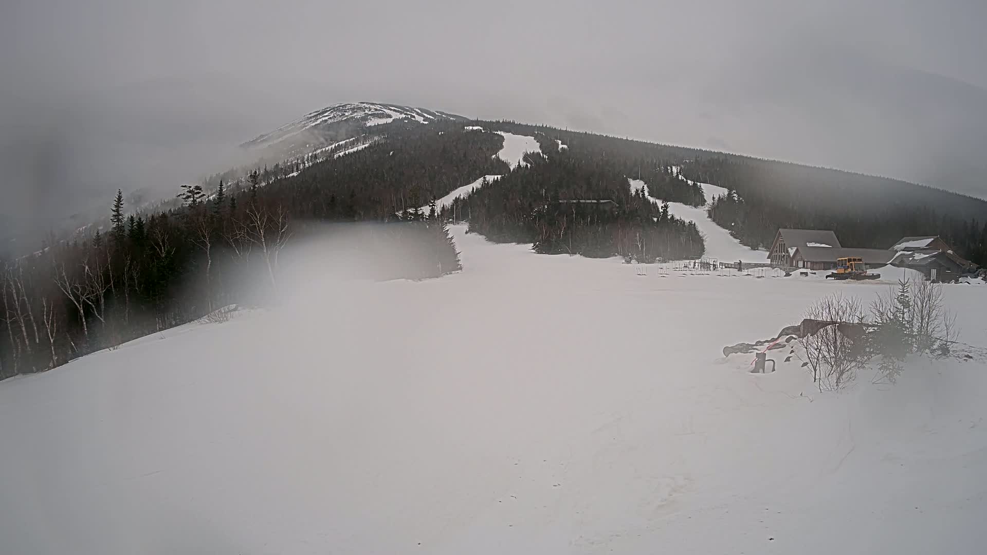 A snow-covered ski resort with a mountain in the background is shrouded in fog.