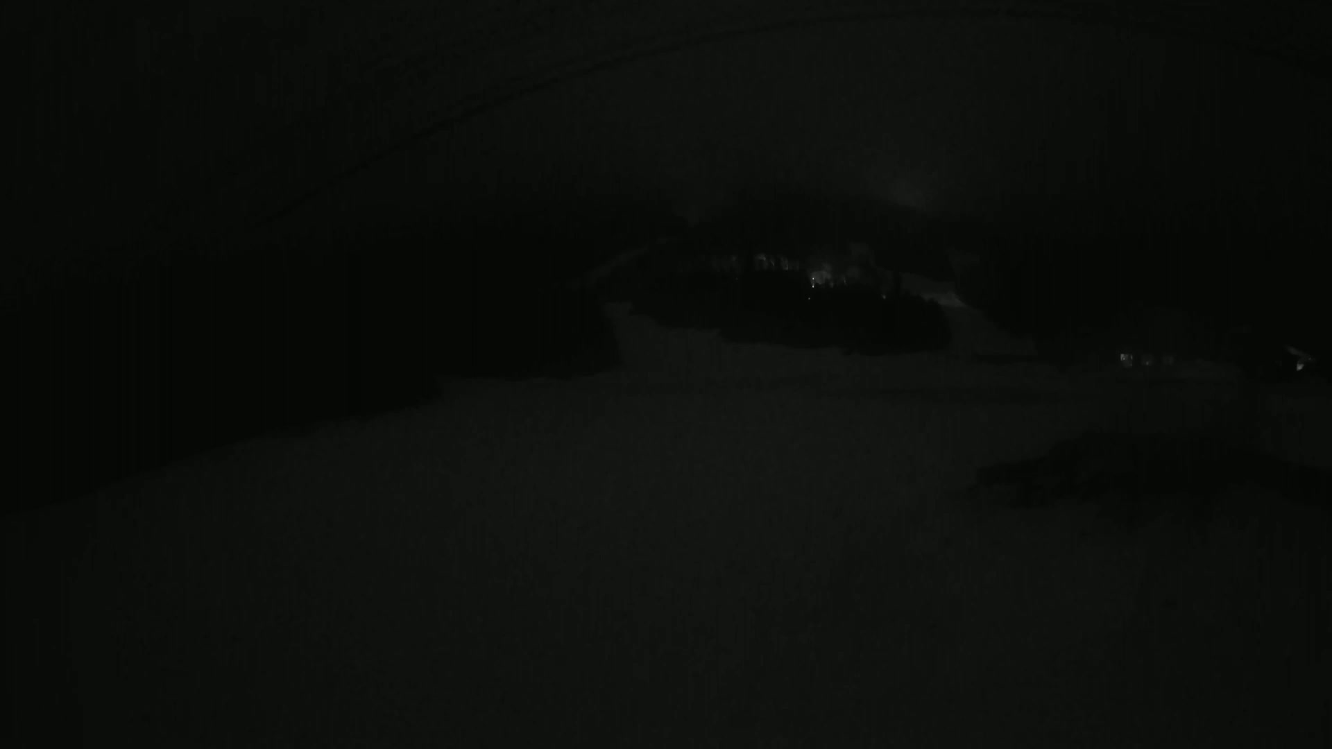 A dark, snowy landscape is visible at night, with faintly lit buildings in the distance.
