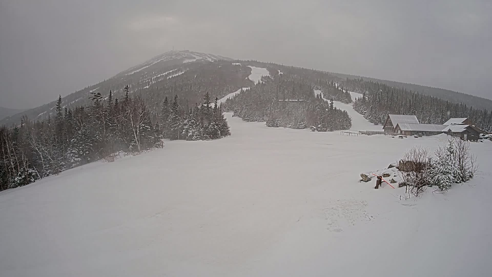 A snow-covered mountain with ski slopes and a few buildings is visible under a heavy, overcast sky.