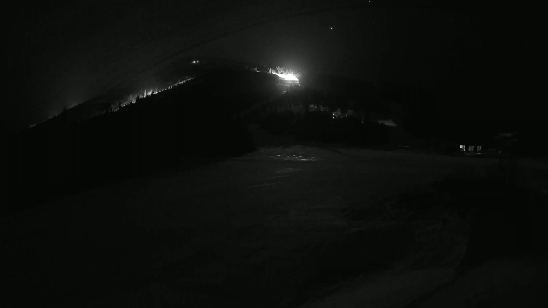 A brightly lit area on a dark, snow-covered hillside is visible under a clear night sky.