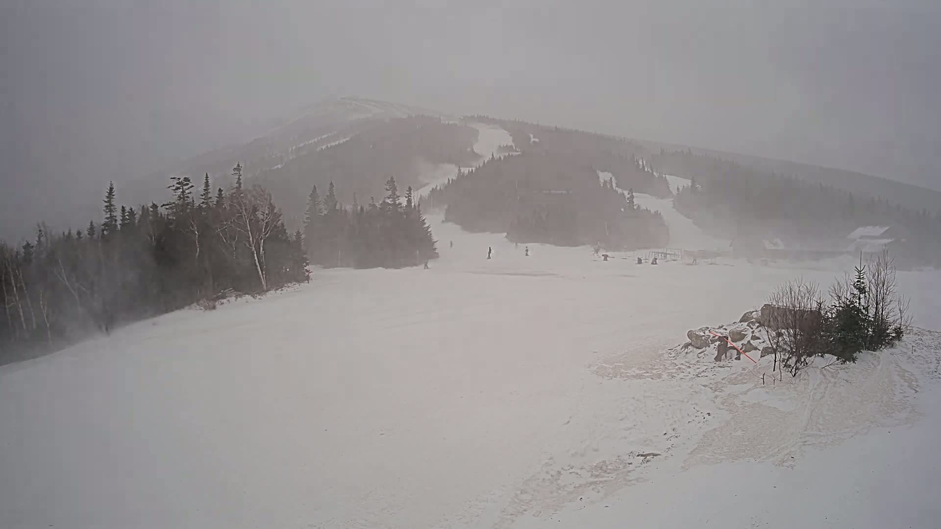 A snow-covered ski slope is visible below a snow-covered mountain during a heavy snowstorm.