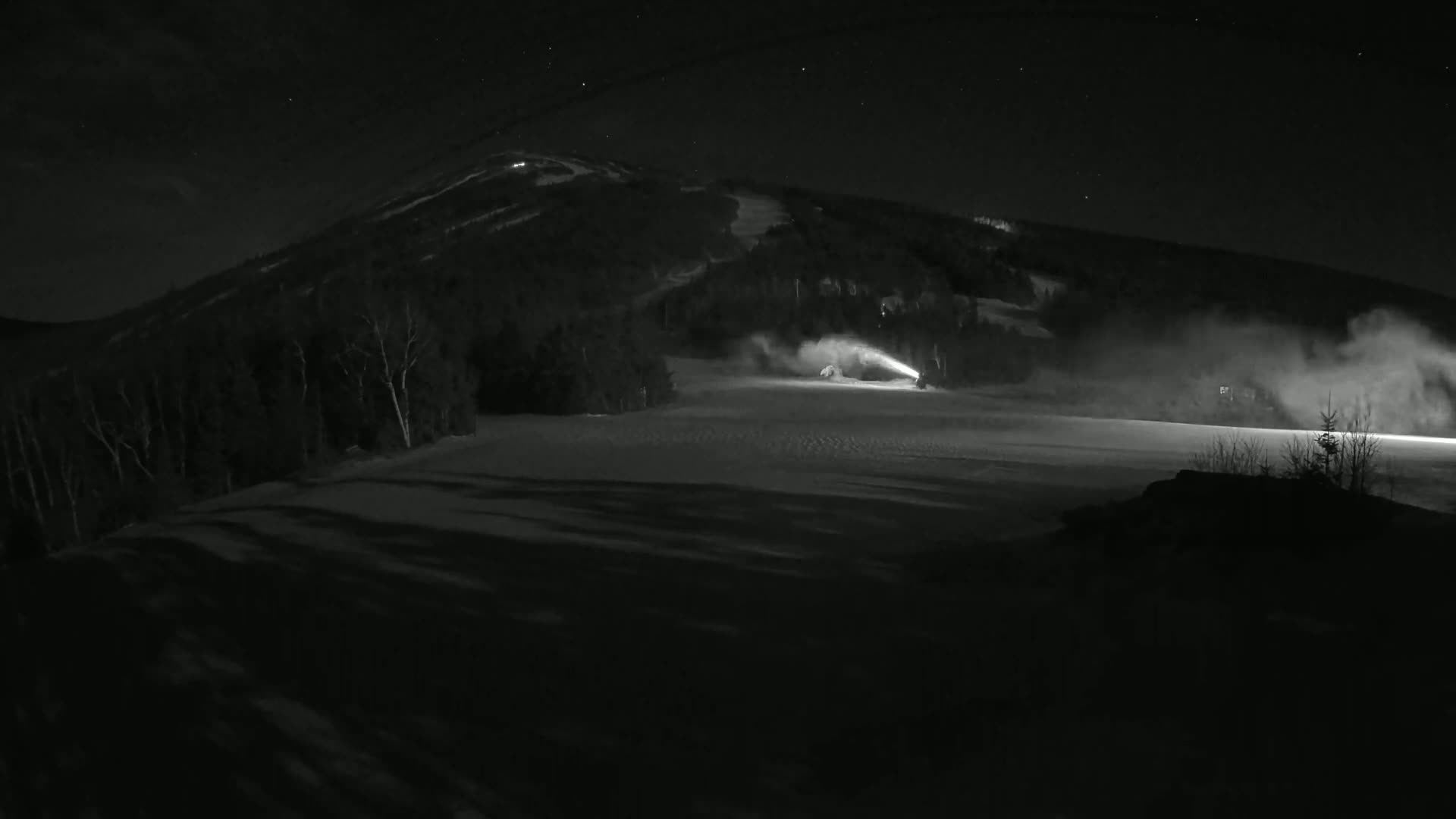 Snow cannons illuminate a snow-covered ski slope at night under a starry sky.