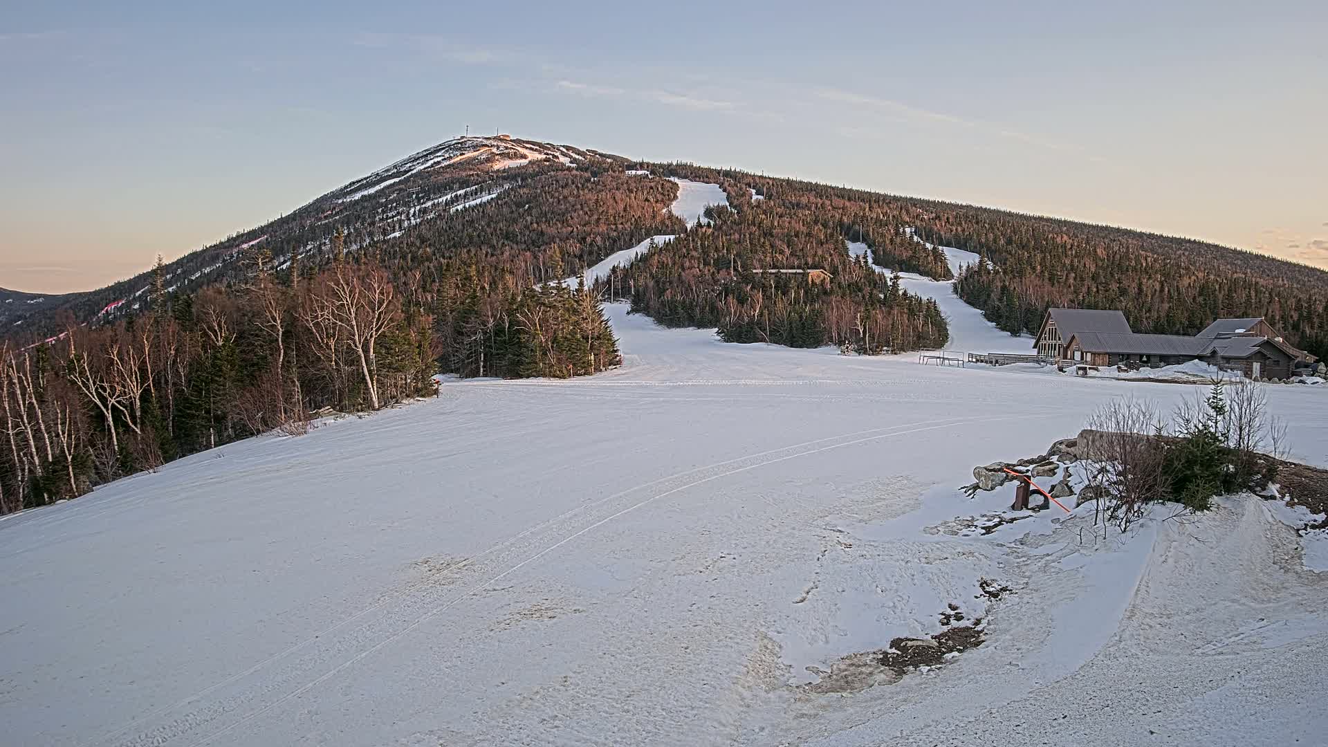 A snow-covered ski resort with a building at the base of a mountain under a twilight sky.