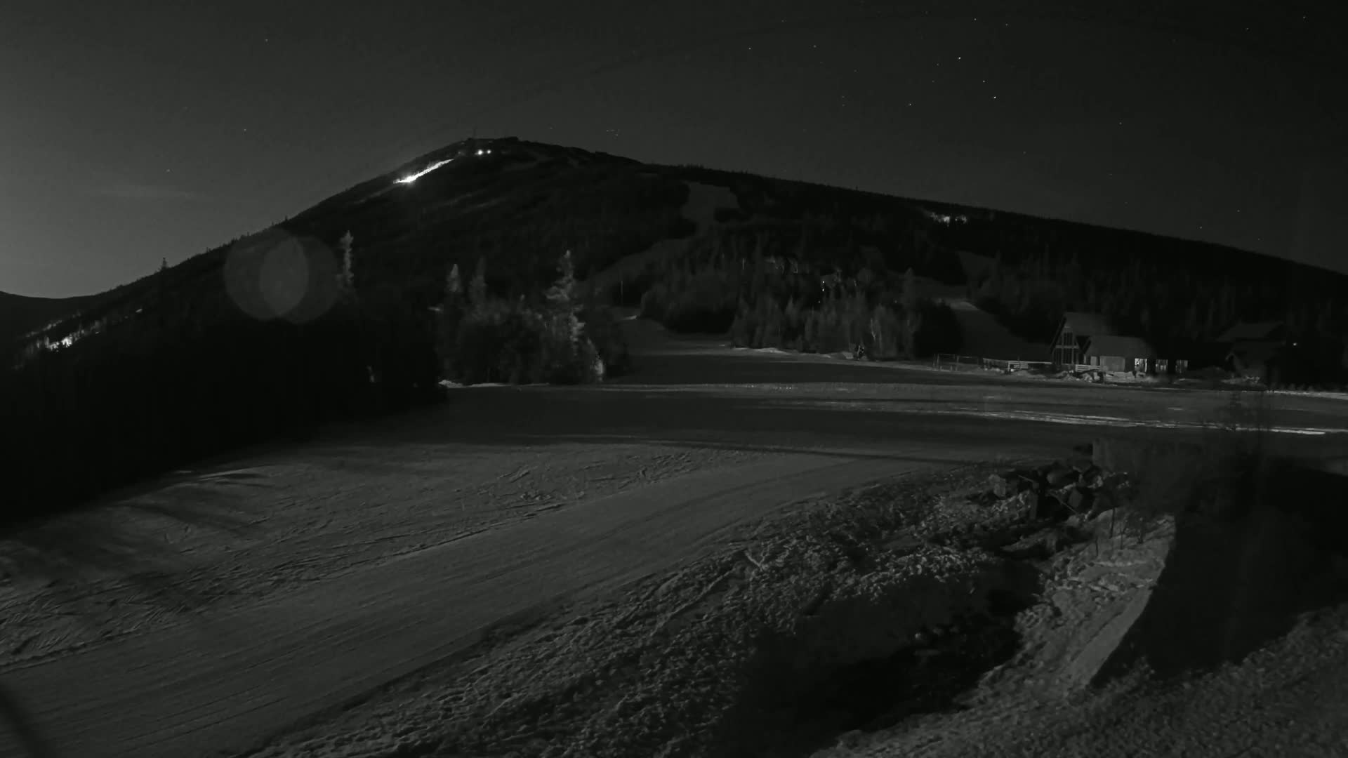 A snow-covered ski slope at night under a starry sky, with a mountain illuminated in the background.