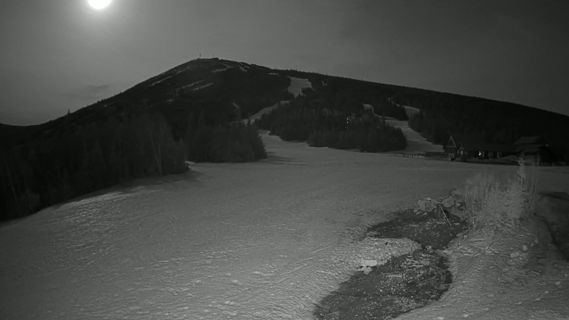 A snow-covered ski slope at night is illuminated by a bright moon.