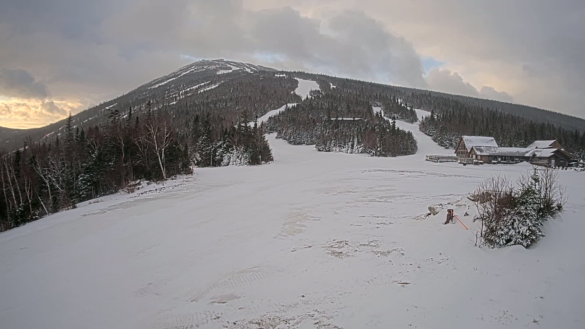A snow-covered ski resort with a mountain in the background under a cloudy sky.