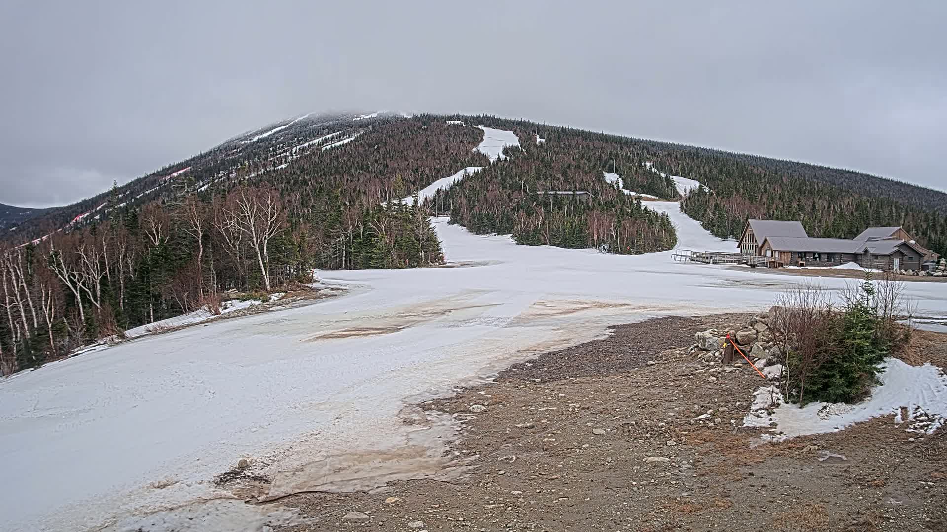 A snow-covered ski slope with a lodge at its base is visible under an overcast sky.