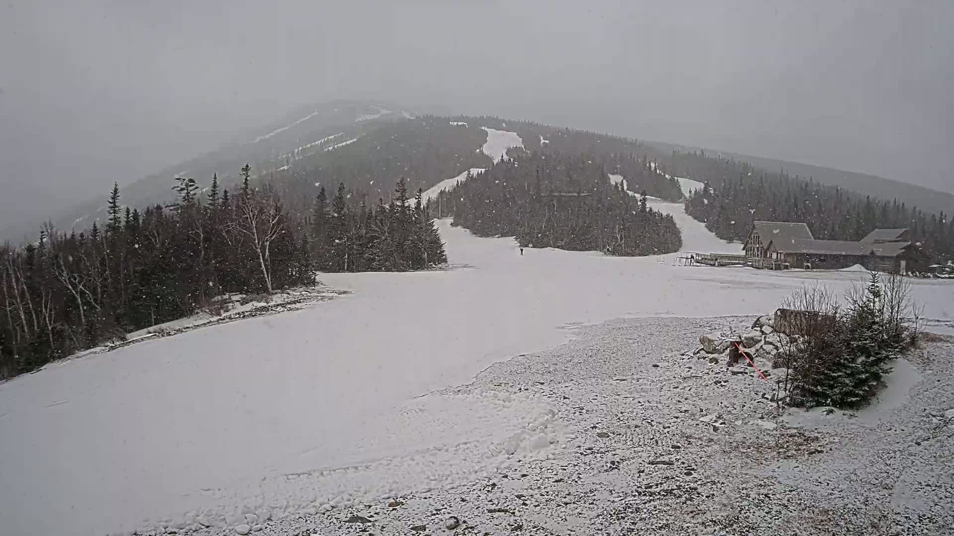 A snow-covered ski slope with a building at the base is seen under heavy snowfall.