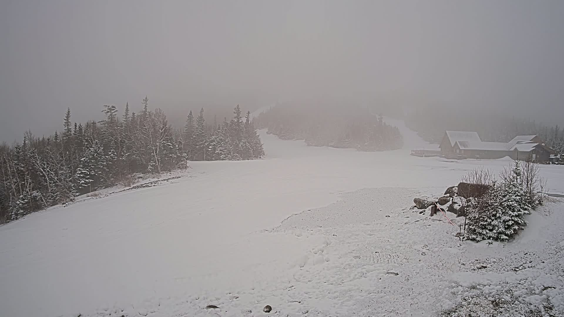A snow-covered landscape with a few buildings in the distance, under a heavy fog.