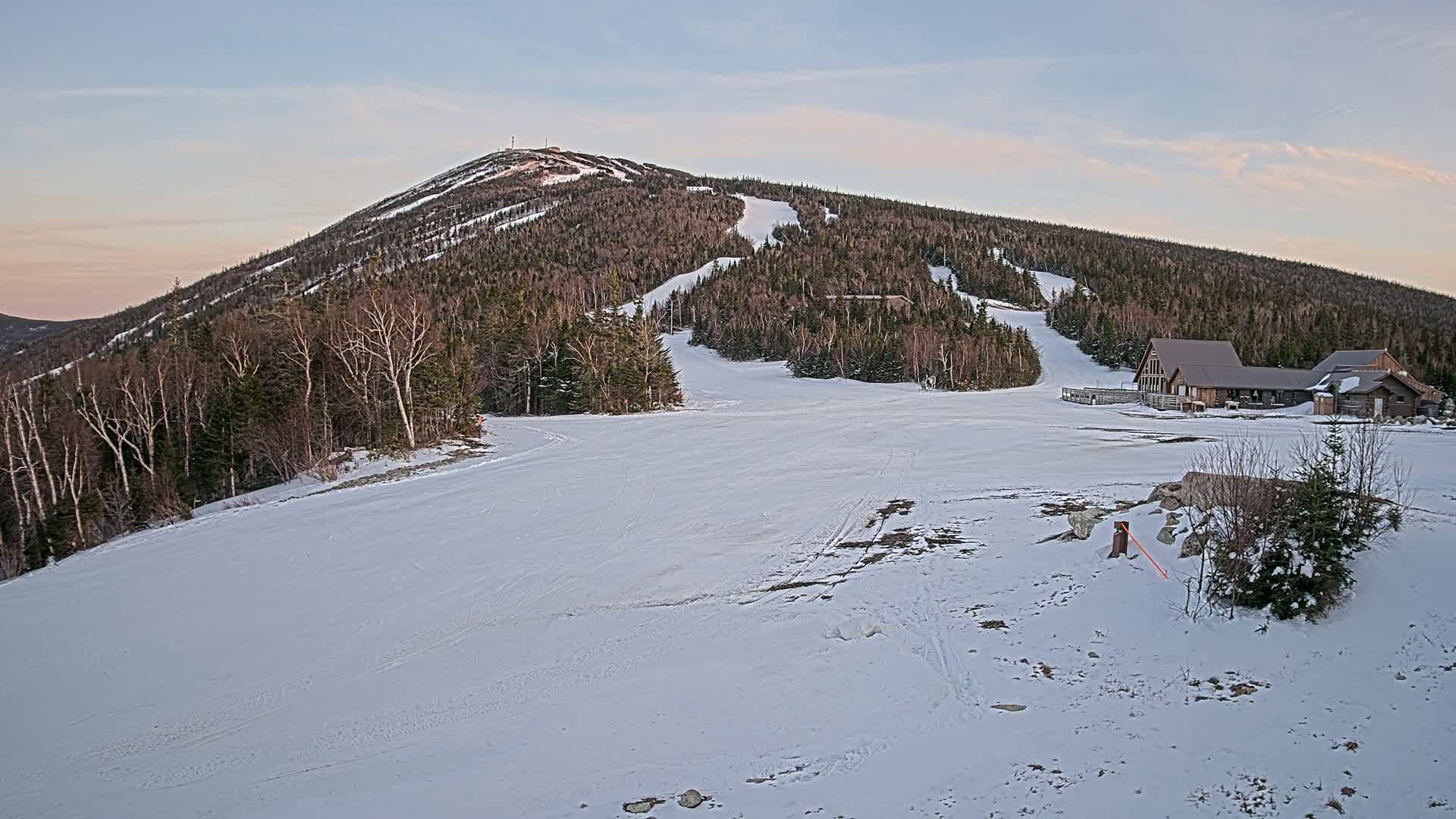 A snow-covered ski slope with a mountain in the background under a twilight sky.