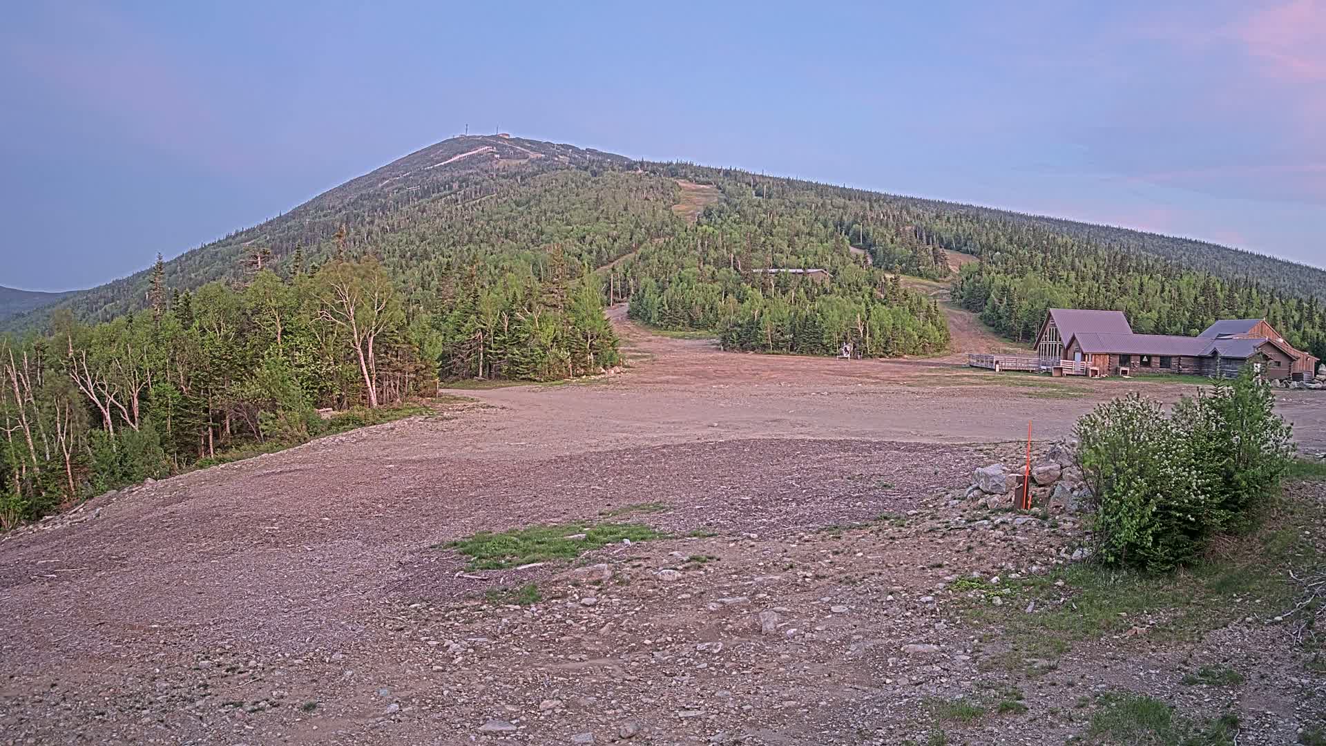 A large, tree-covered mountain with a ski resort at its base is visible under a clear, twilight sky.