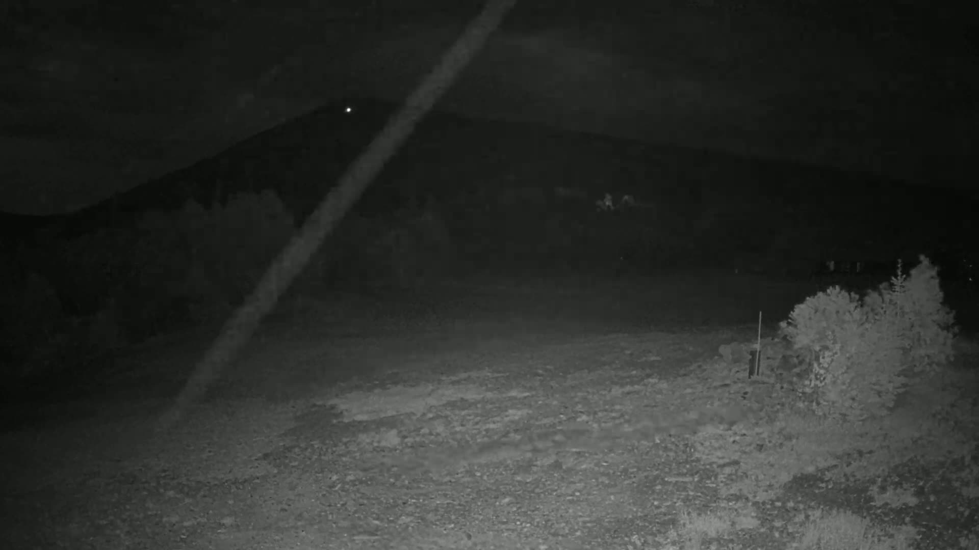 A nighttime, low-light image shows a dark, rocky ground leading to a hill silhouetted against a dark sky.