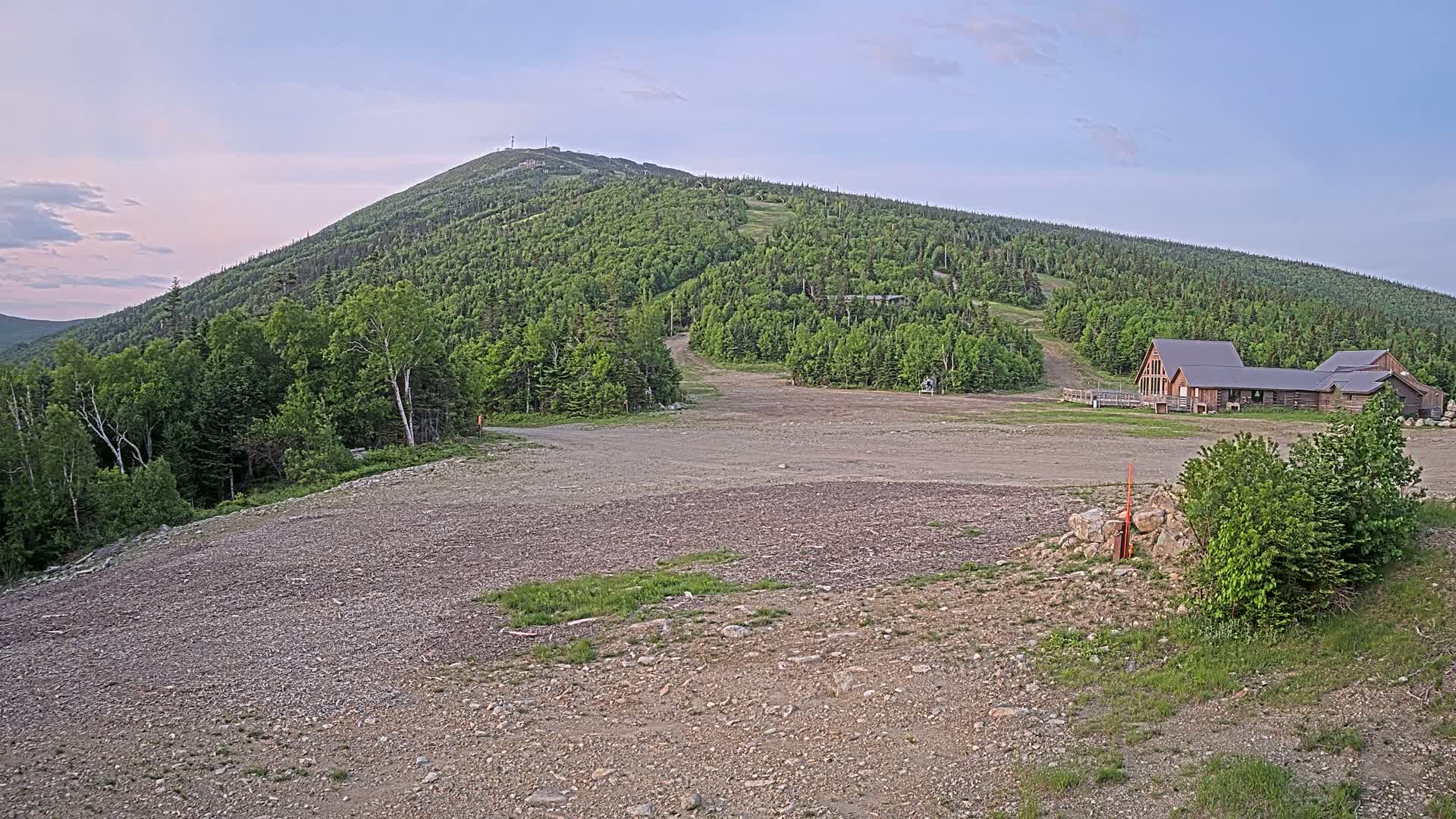 A large, grassy mountain with a ski resort building at its base is visible under a clear, twilight sky.
