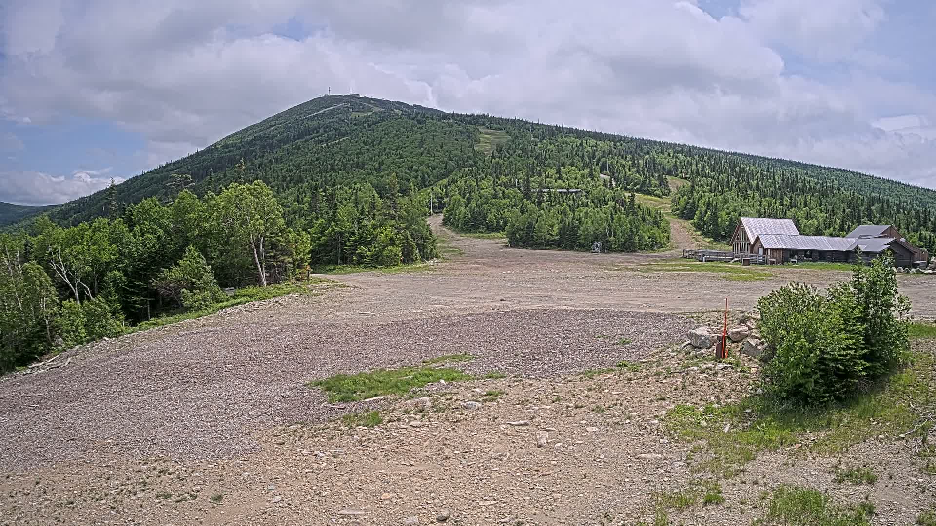 A rocky, mostly barren expanse at the base of a large, forested mountain under a partly cloudy sky.