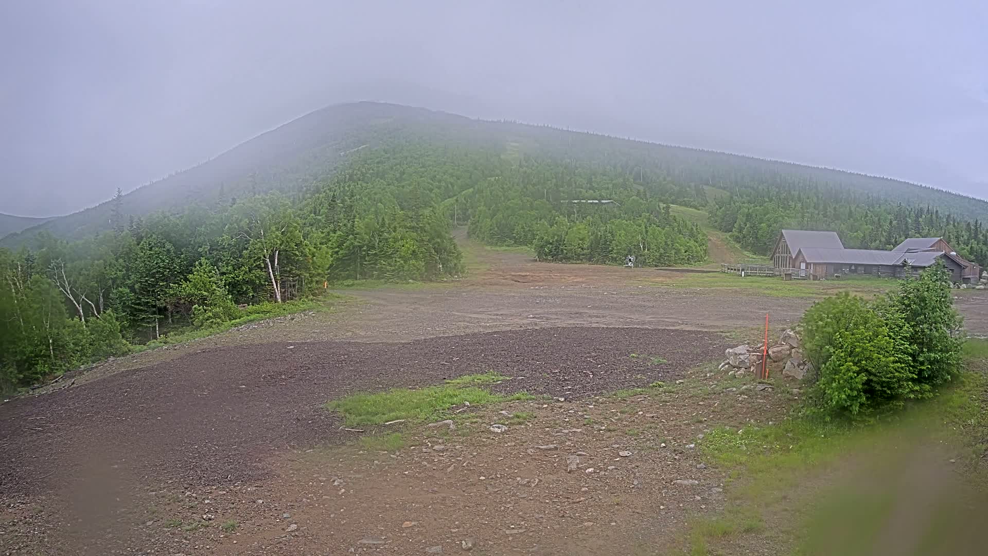 A mostly clear view of a mountain covered in a lush green forest with a building at its base on a foggy day.