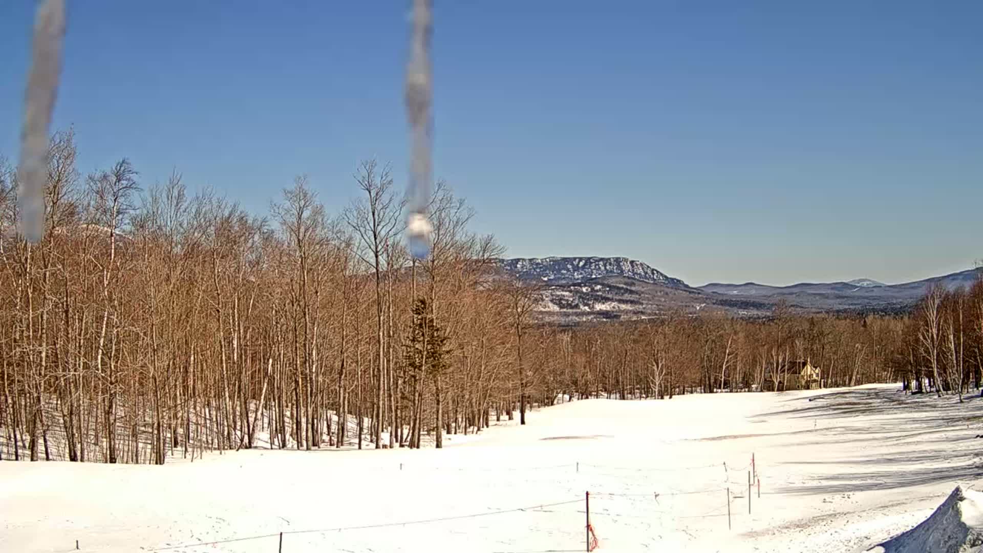 A snow-covered landscape with bare trees and distant mountains under a clear blue sky is visible, with icicles hanging in the foreground.