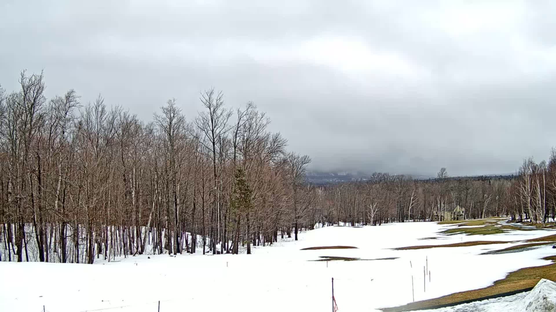 A snow-covered golf course is nestled among leafless trees under a cloudy sky.