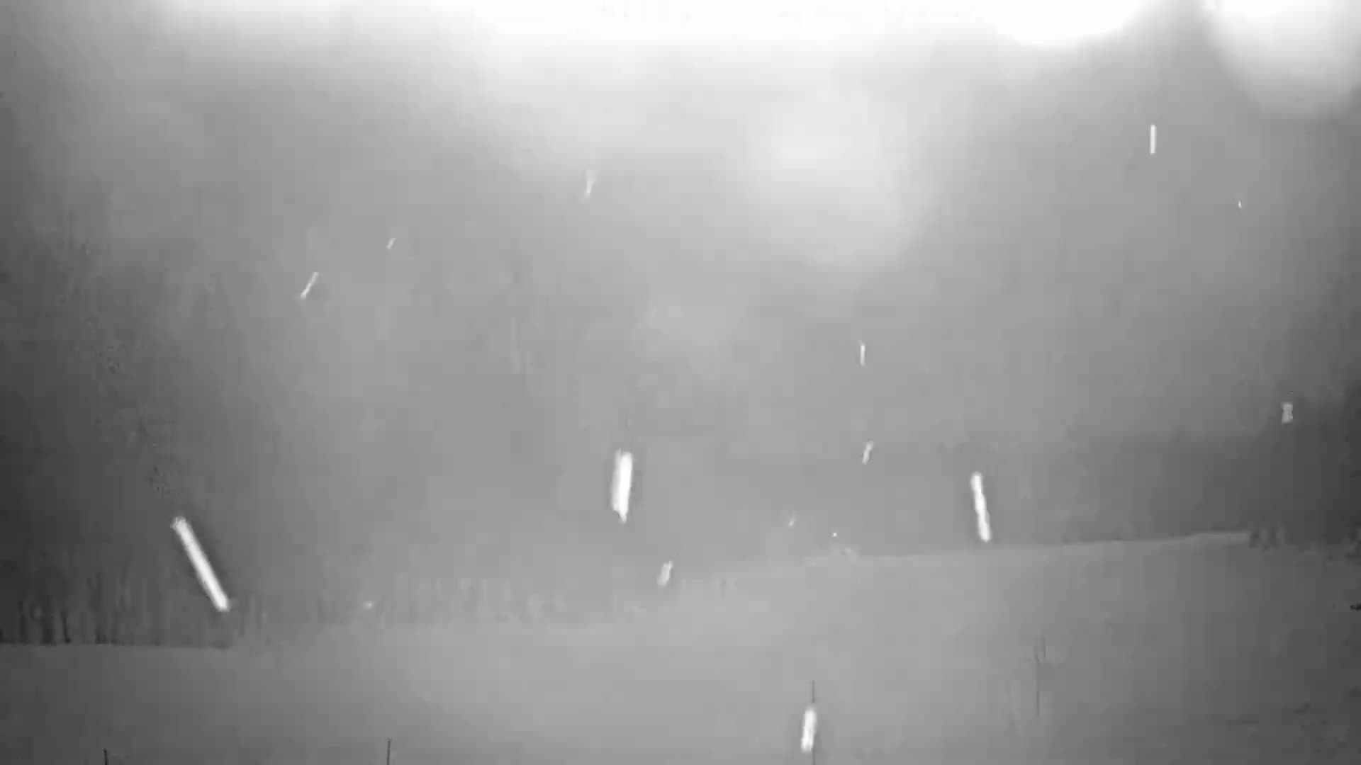 A snowy landscape is visible through a hazy atmosphere, with falling snow obscuring the view of distant trees and structures.