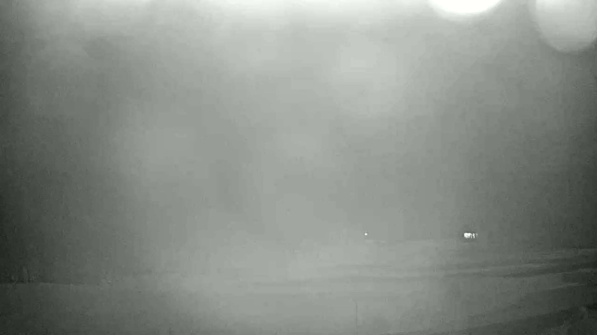 A hazy, possibly foggy, nighttime scene shows a flat, indistinct landscape with a few faint lights in the distance.
