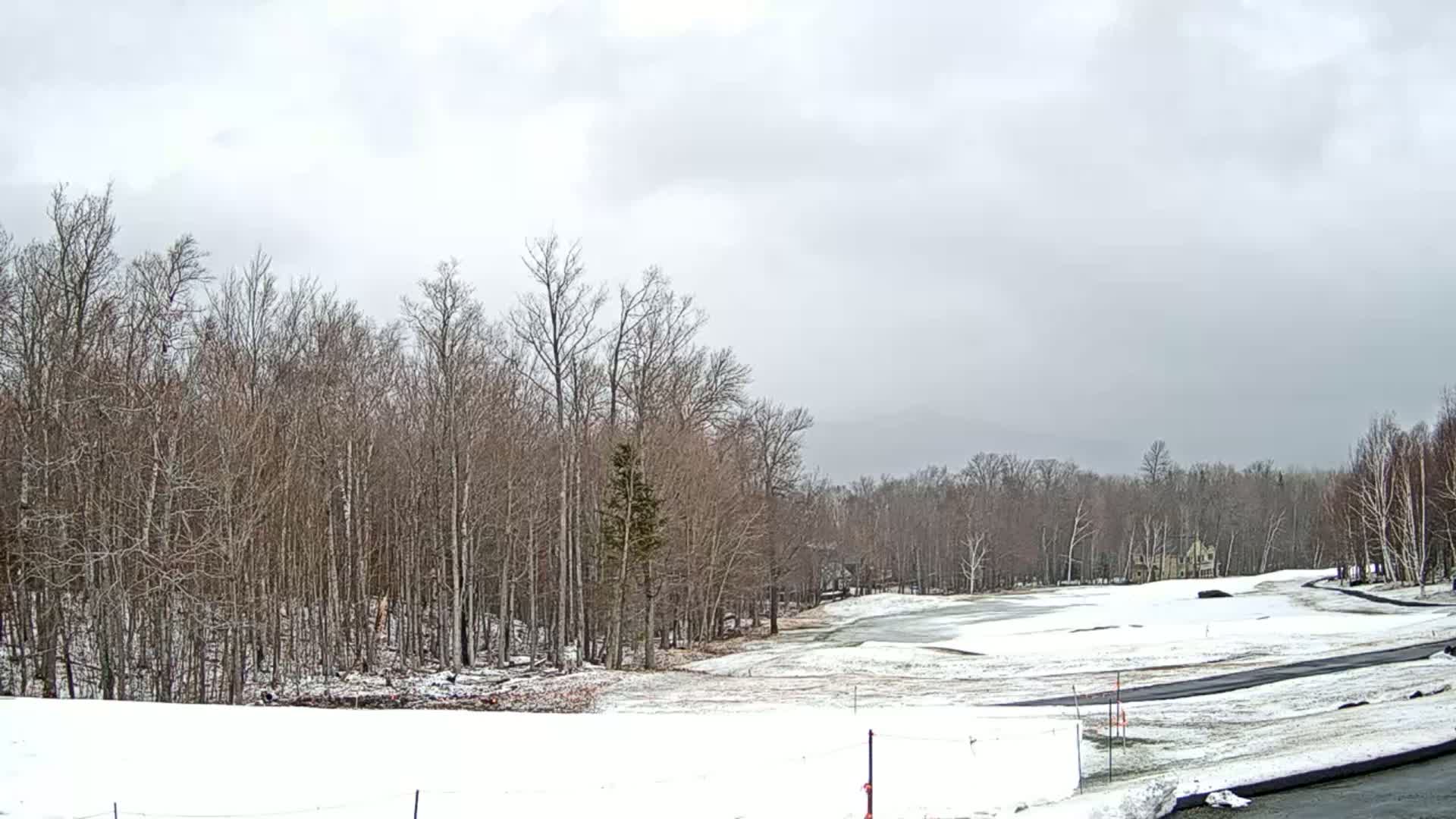 A snow-covered golf course is nestled amongst leafless trees under a cloudy sky.