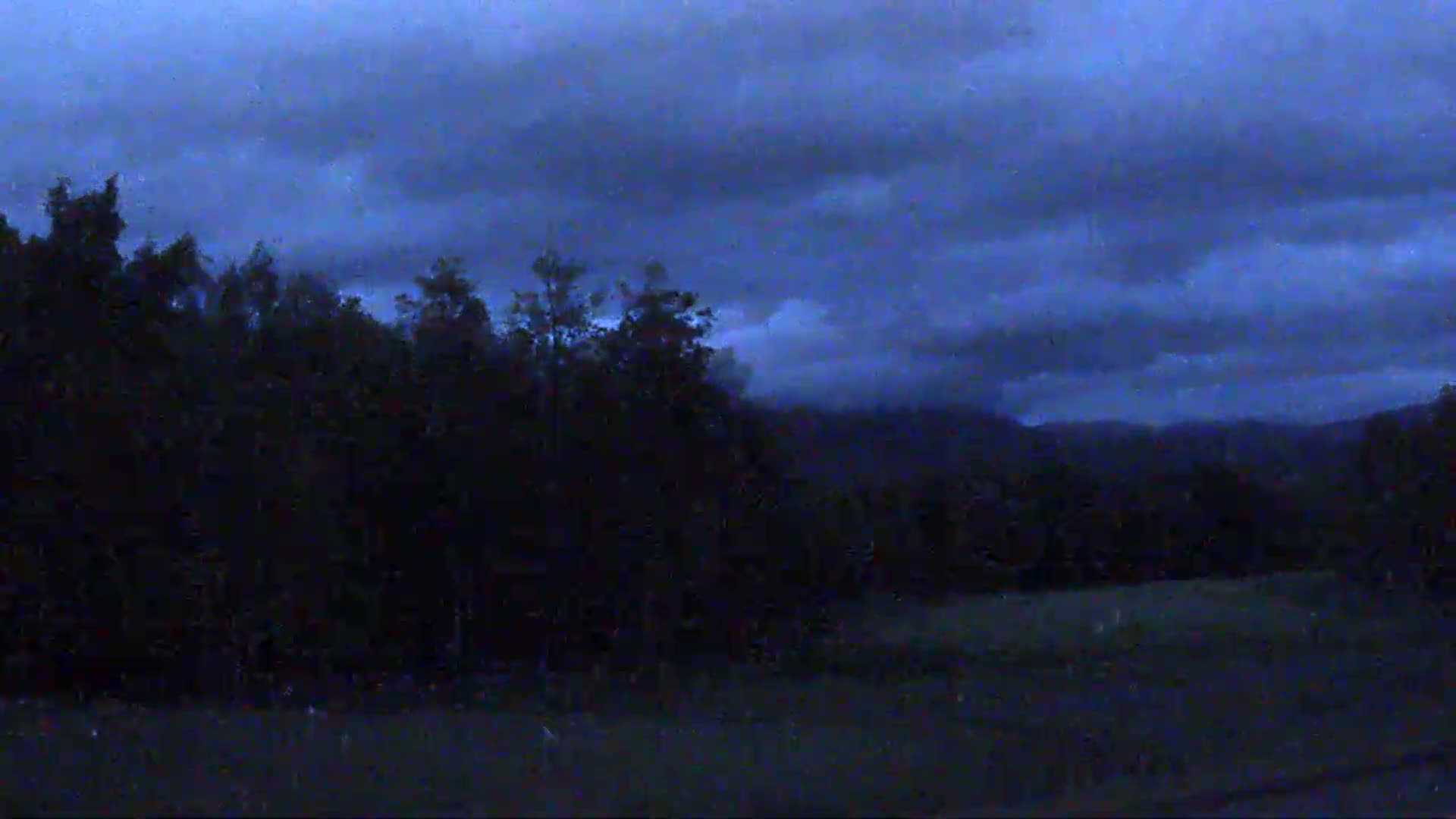 A dark, overcast sky hangs over a silhouetted line of trees and distant mountains.