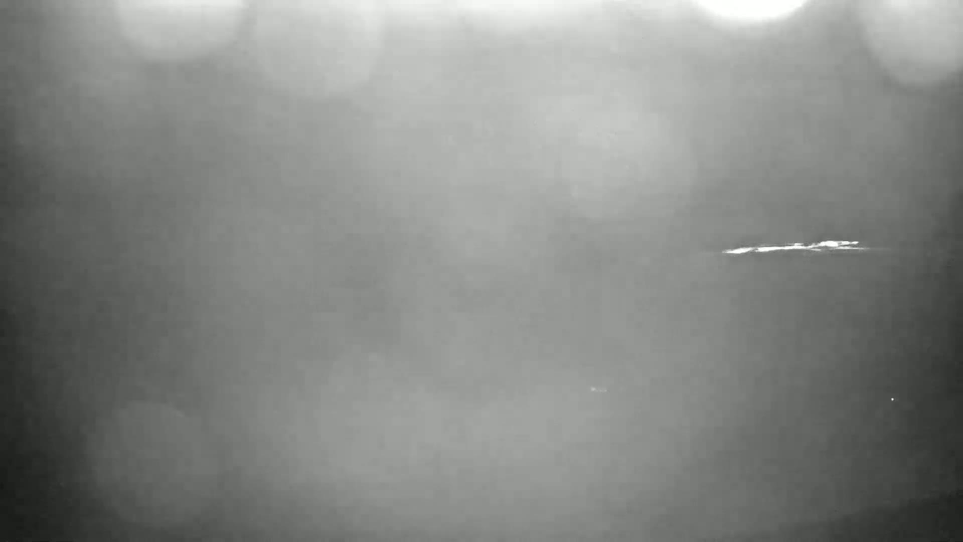 A blurry, low-light image shows a faint, horizontal line possibly representing land or a body of water under hazy or foggy conditions.