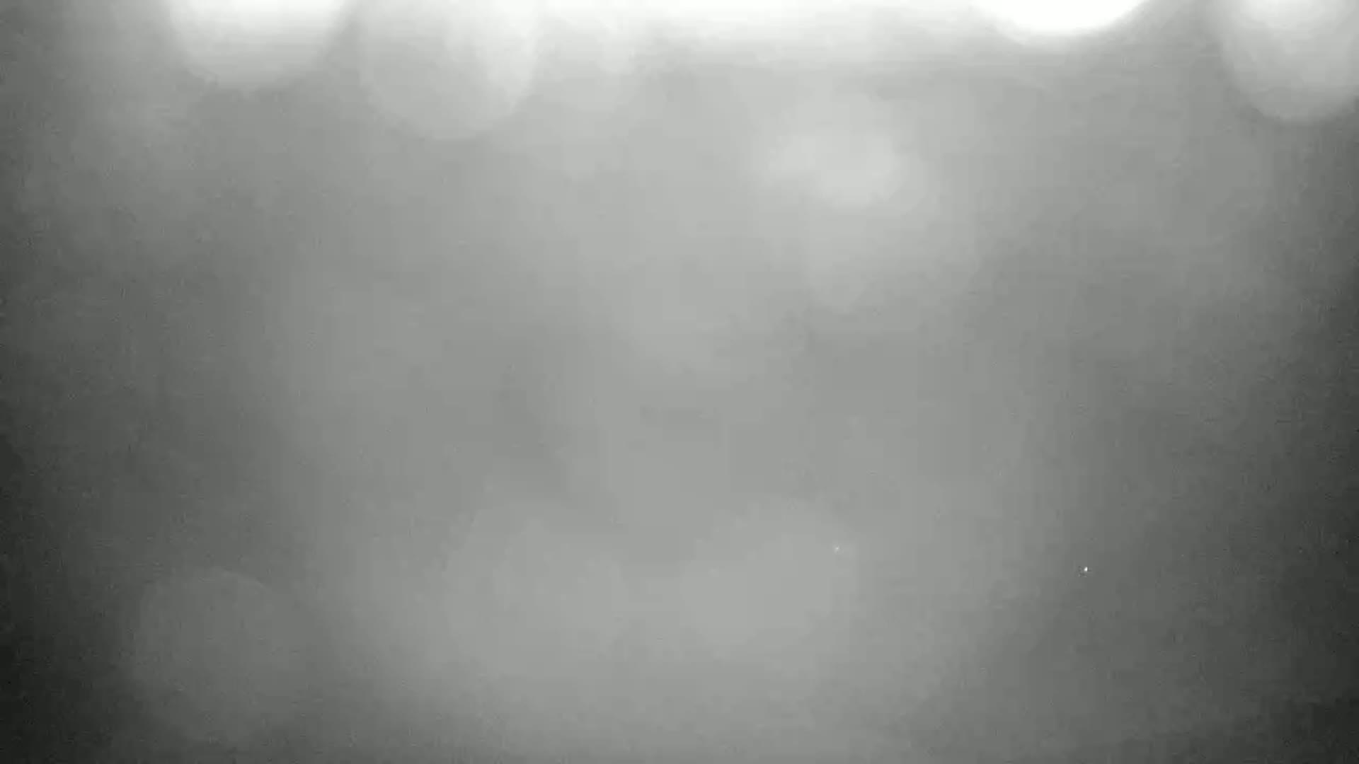 A blurry, out-of-focus image shows a foggy or hazy outdoor scene with bright, indistinct lights in the background.