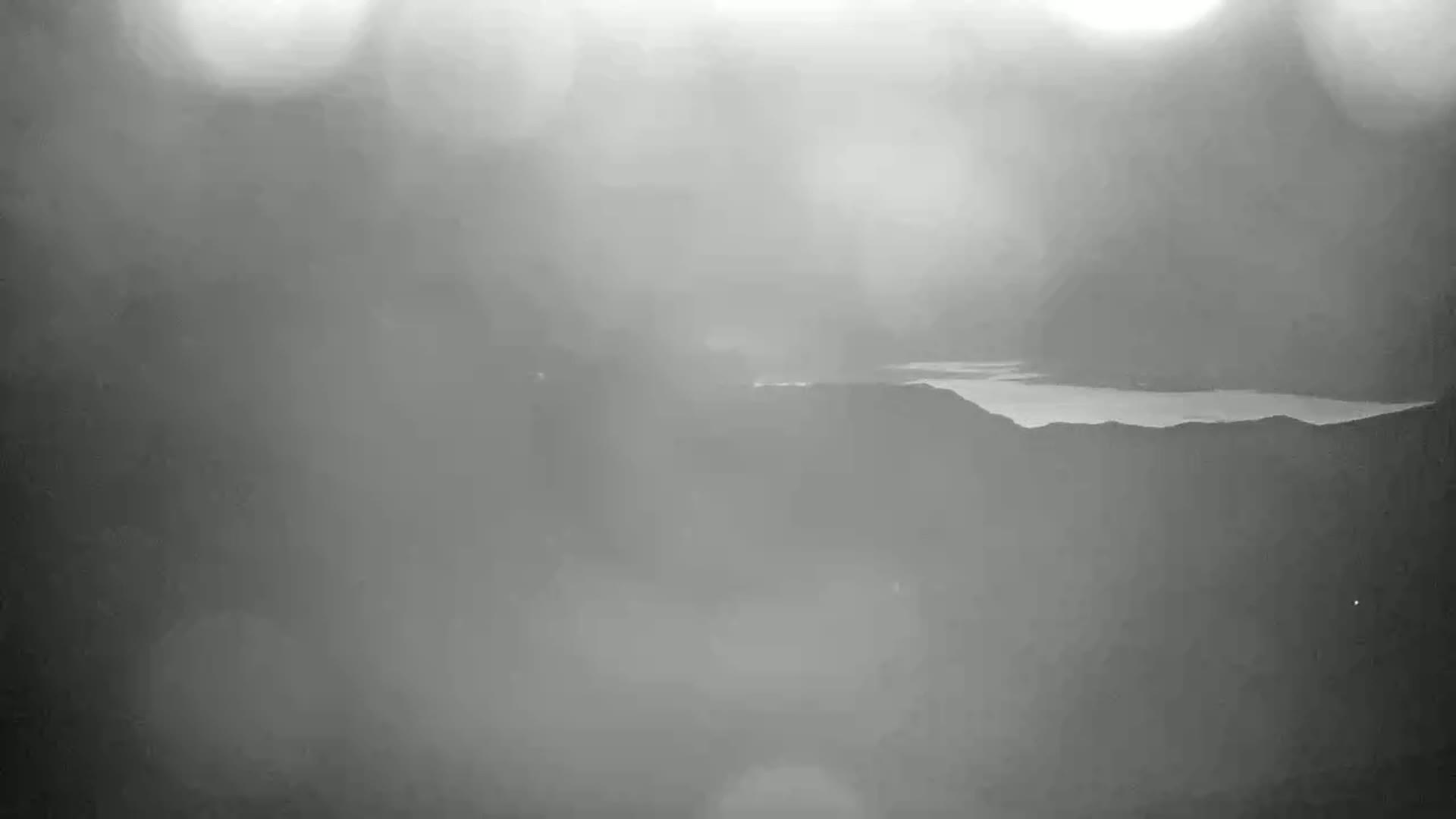 A hazy, gray landscape shows a body of water nestled between dark hills.
