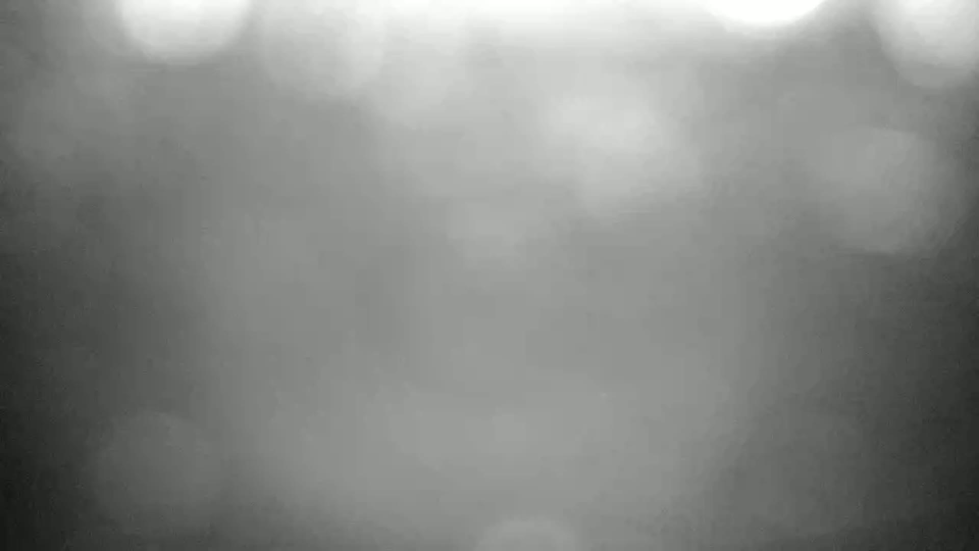 A blurry, out-of-focus grayscale image shows a hazy or foggy scene with bright spots of light.