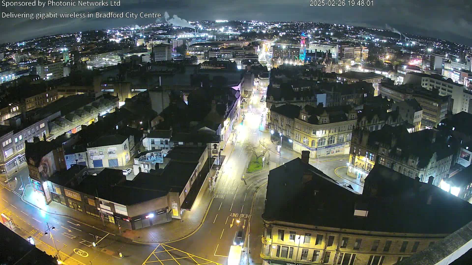 A nighttime aerial view of a city center with illuminated streets and buildings under a clear sky.