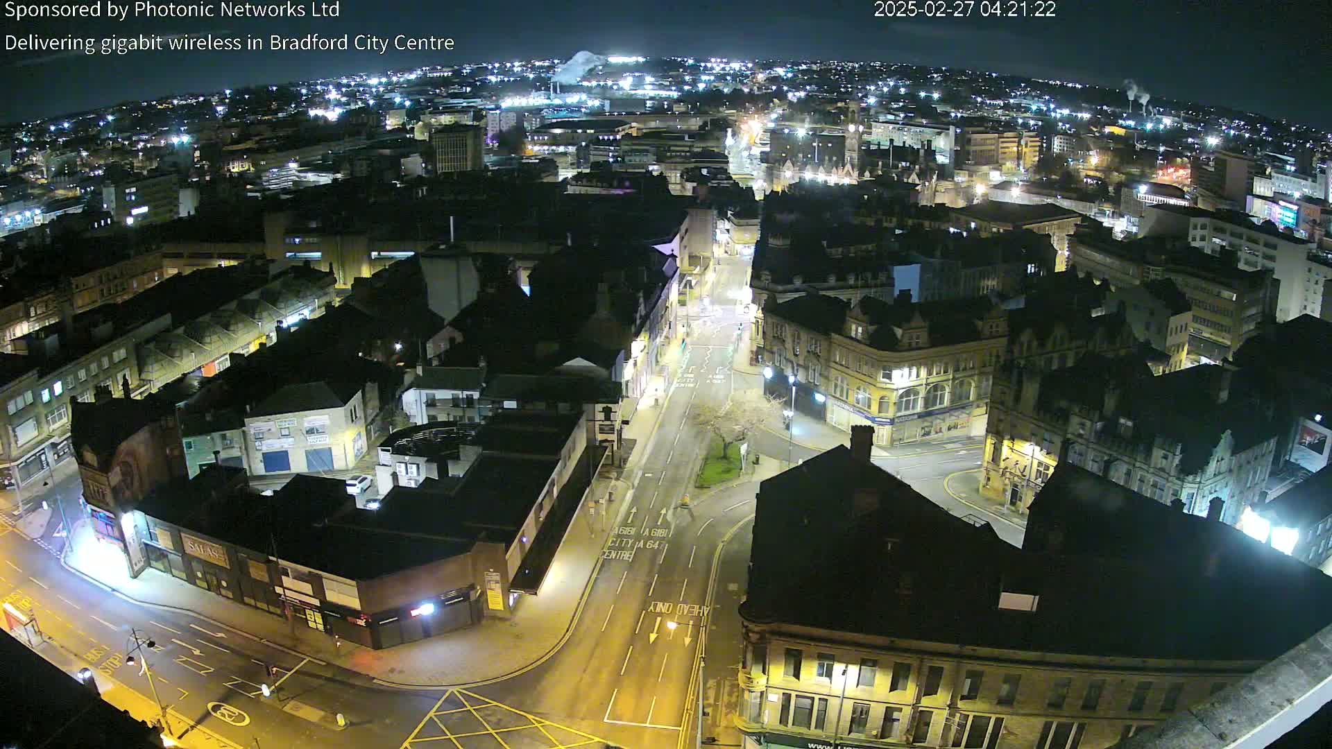 A nighttime, high-angle view of a city center, showing mostly dark buildings with scattered lights and empty streets.