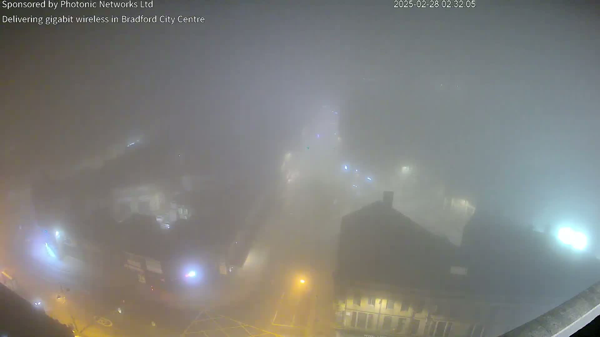 A high-angle, nighttime view of a city shrouded in dense fog, with dimly lit buildings and streets barely visible.