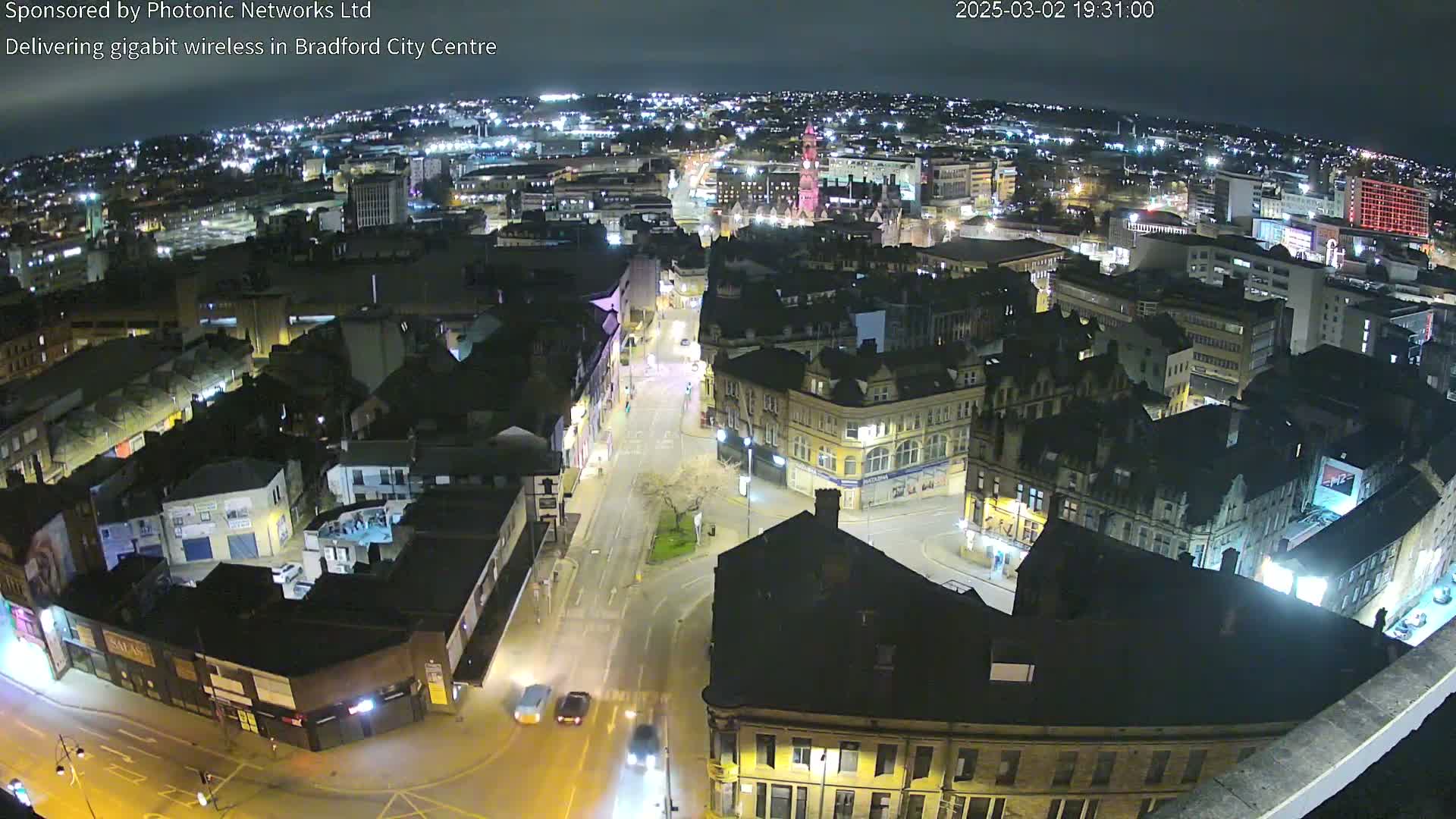 A nighttime aerial view of a city center, showing illuminated buildings and streets with sparse traffic.