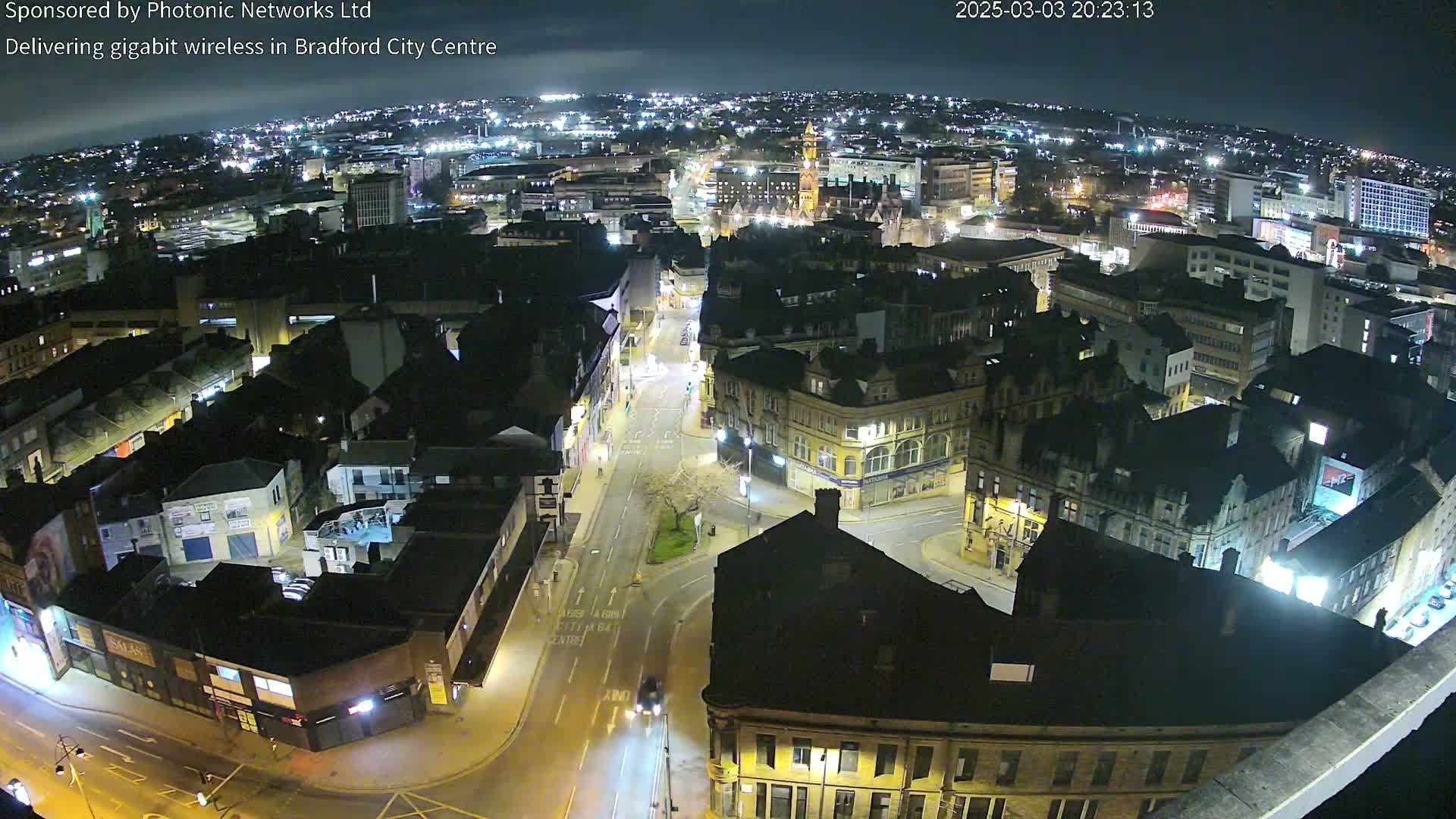 A nighttime aerial view of a city center with illuminated buildings and streets, under a clear, dark sky.