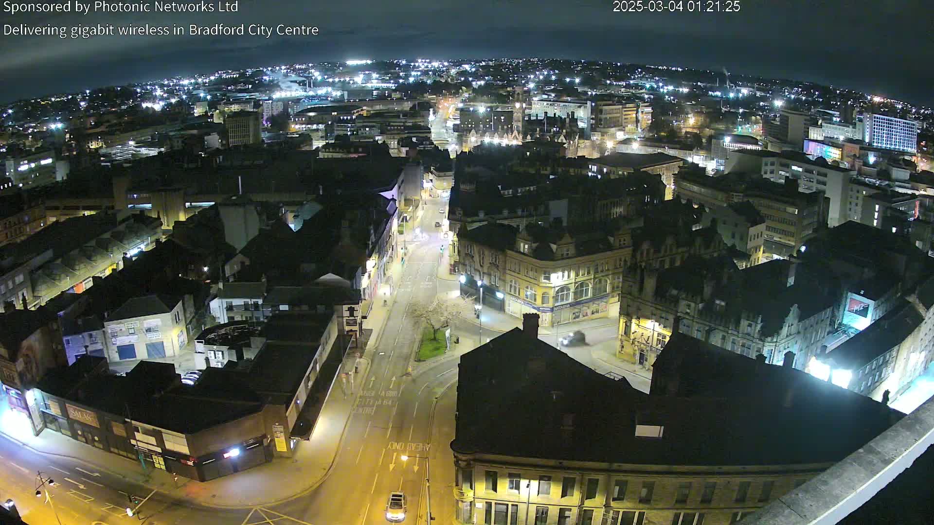 A nighttime aerial view of a city center showing streets, buildings, and sparse vehicle traffic under a clear sky.