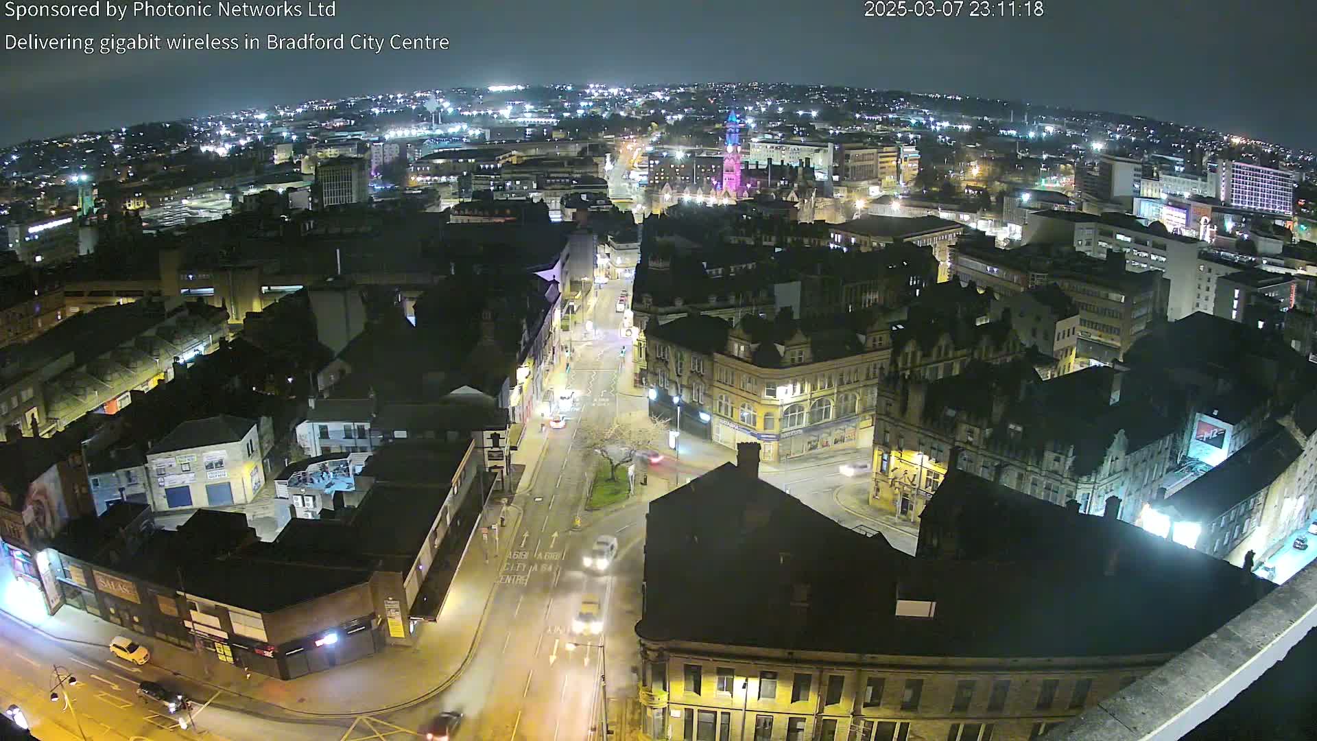 A nighttime aerial view of a city center, showing illuminated streets and buildings under a clear sky.