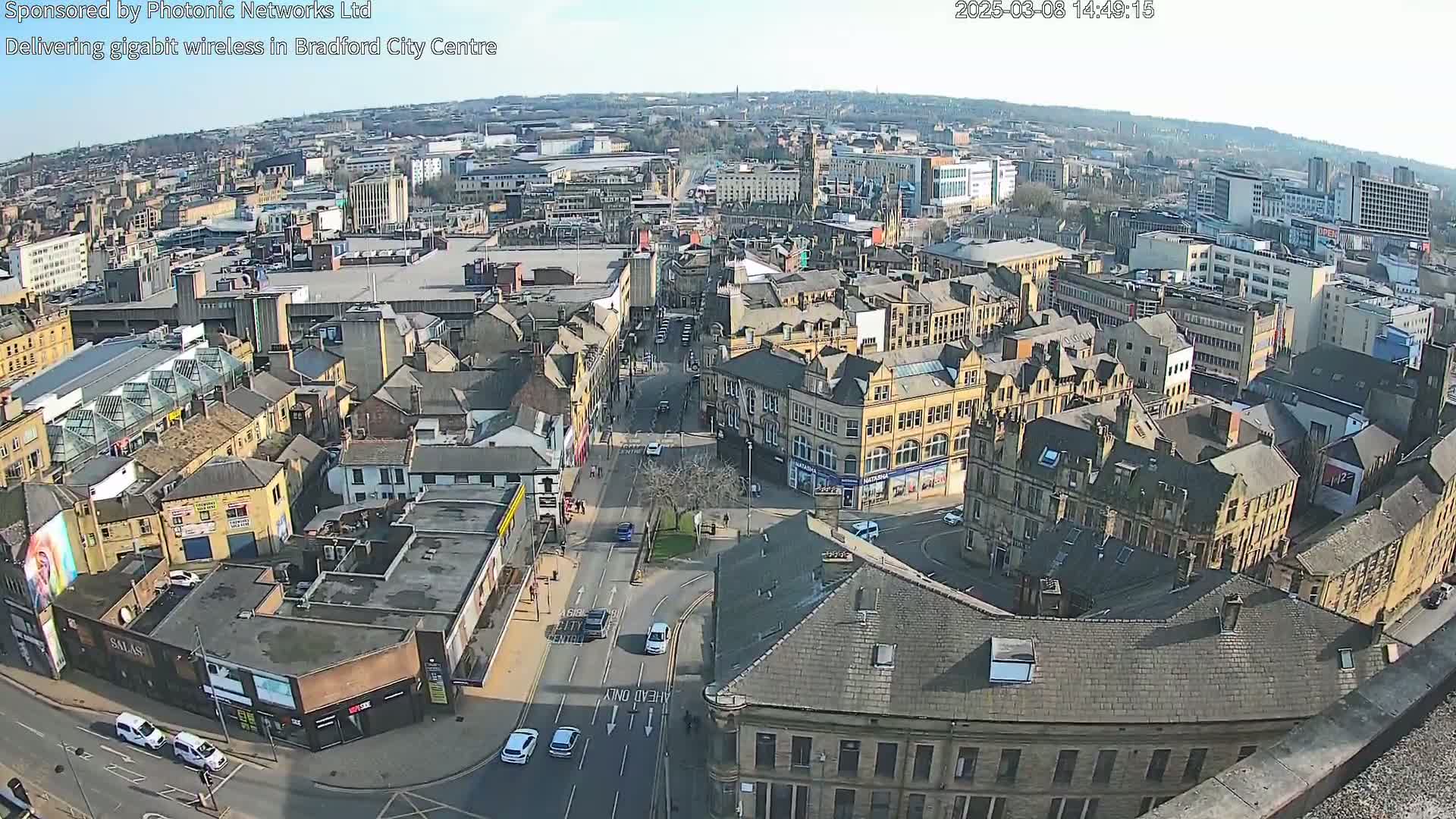 A high-angle, sunny view of a city center with many buildings and sparse traffic on the roads.