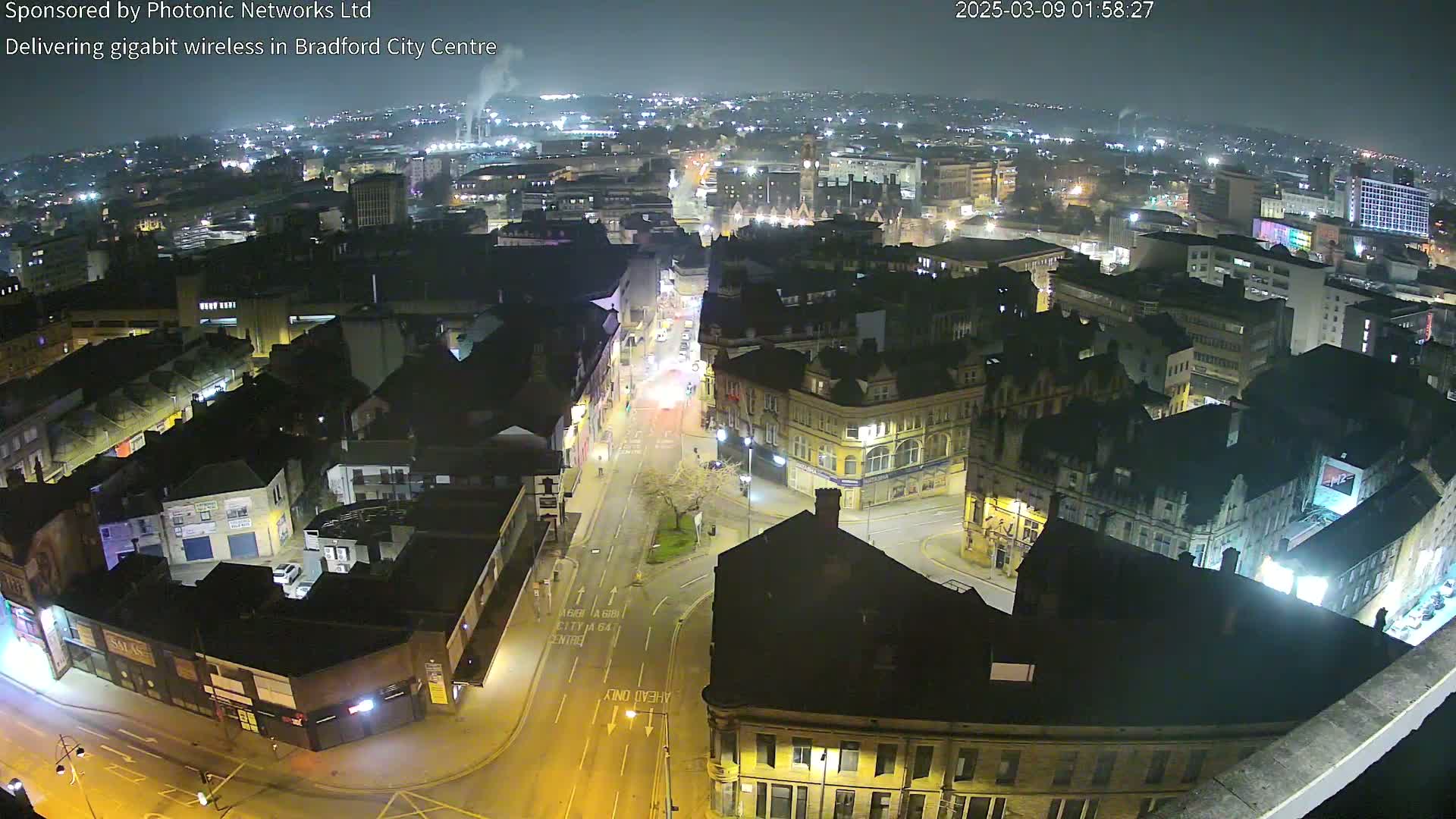 A nighttime aerial view of a city center with illuminated streets and buildings under a clear sky.