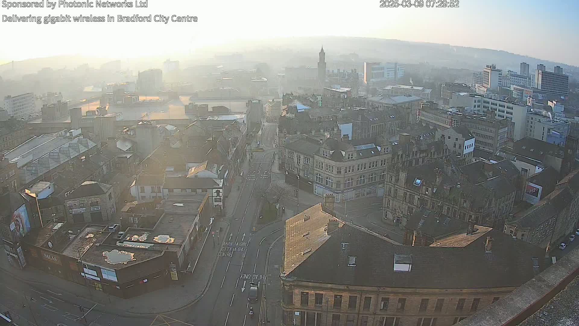A hazy sunrise illuminates a dense cityscape of multi-story buildings, viewed from an elevated perspective.